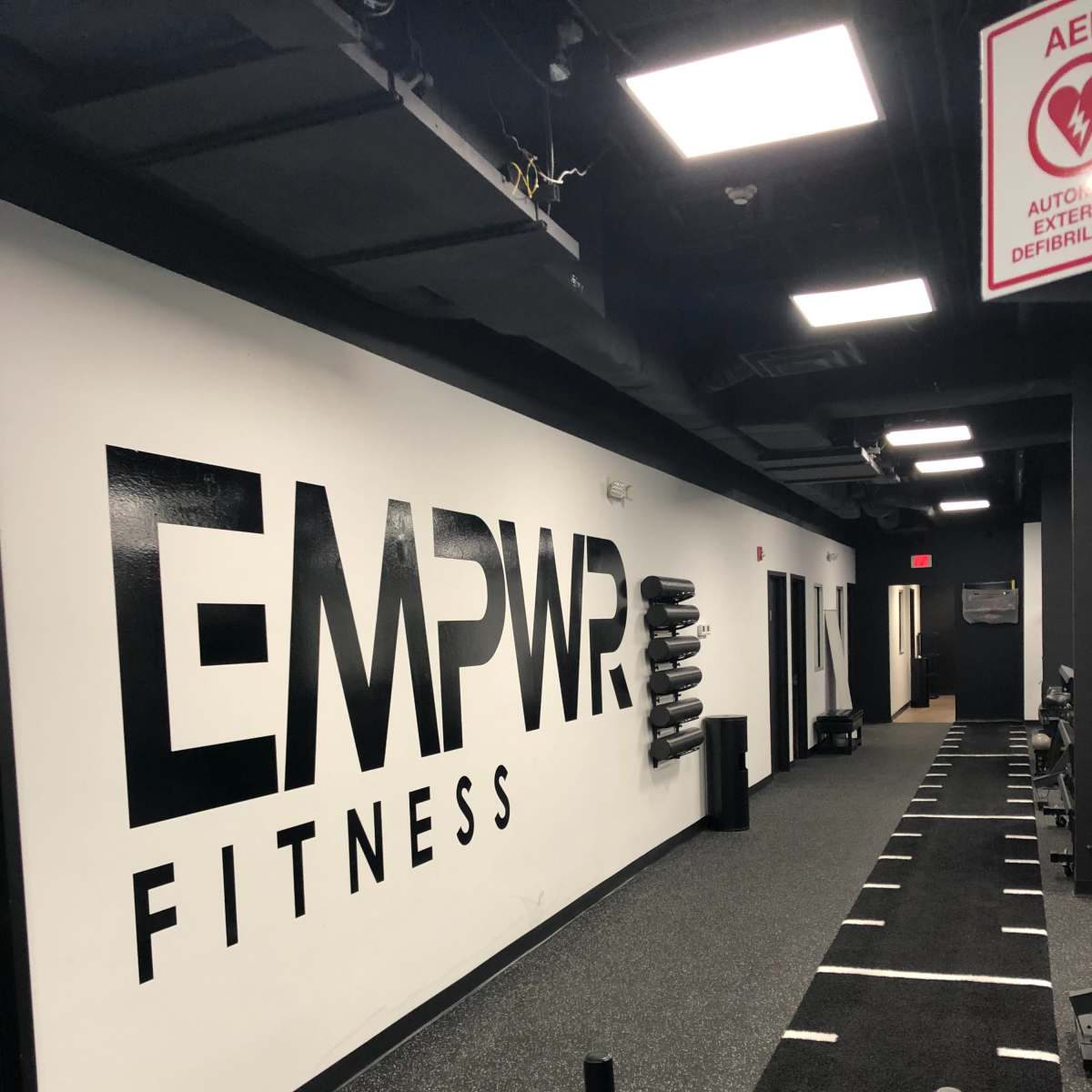 A fitness facility hallway with a large "EMPWR FITNESS" sign on the wall and rubber flooring.