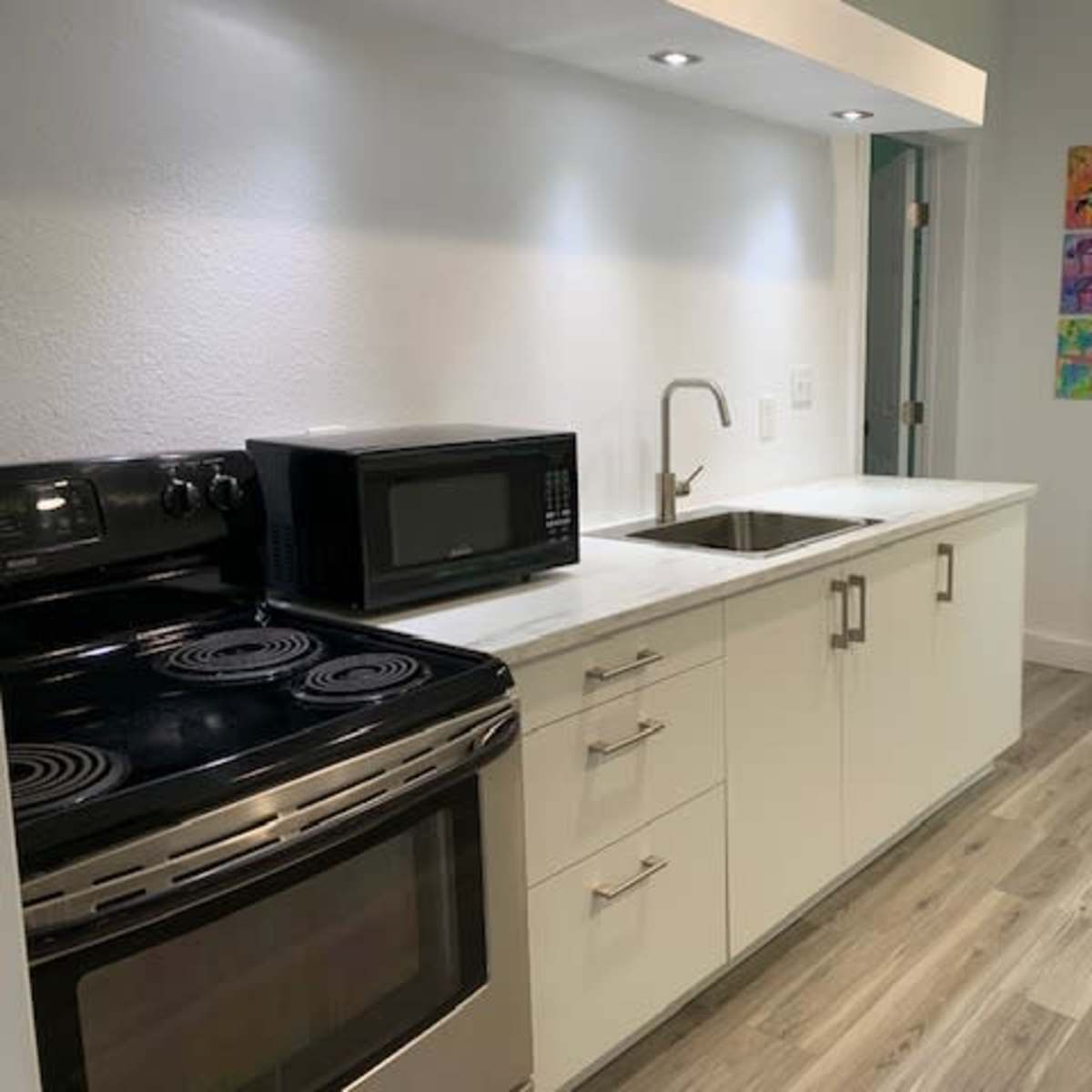 The kitchen features a black stove and microwave, white cabinetry, a stainless steel sink, and light wood flooring.