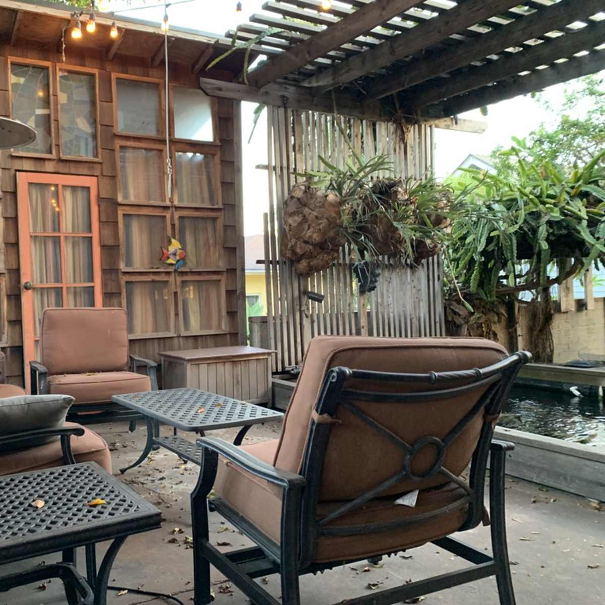 A cozy outdoor seating area features brown metal-framed chairs and a table, surrounded by a wooden structure and greenery.