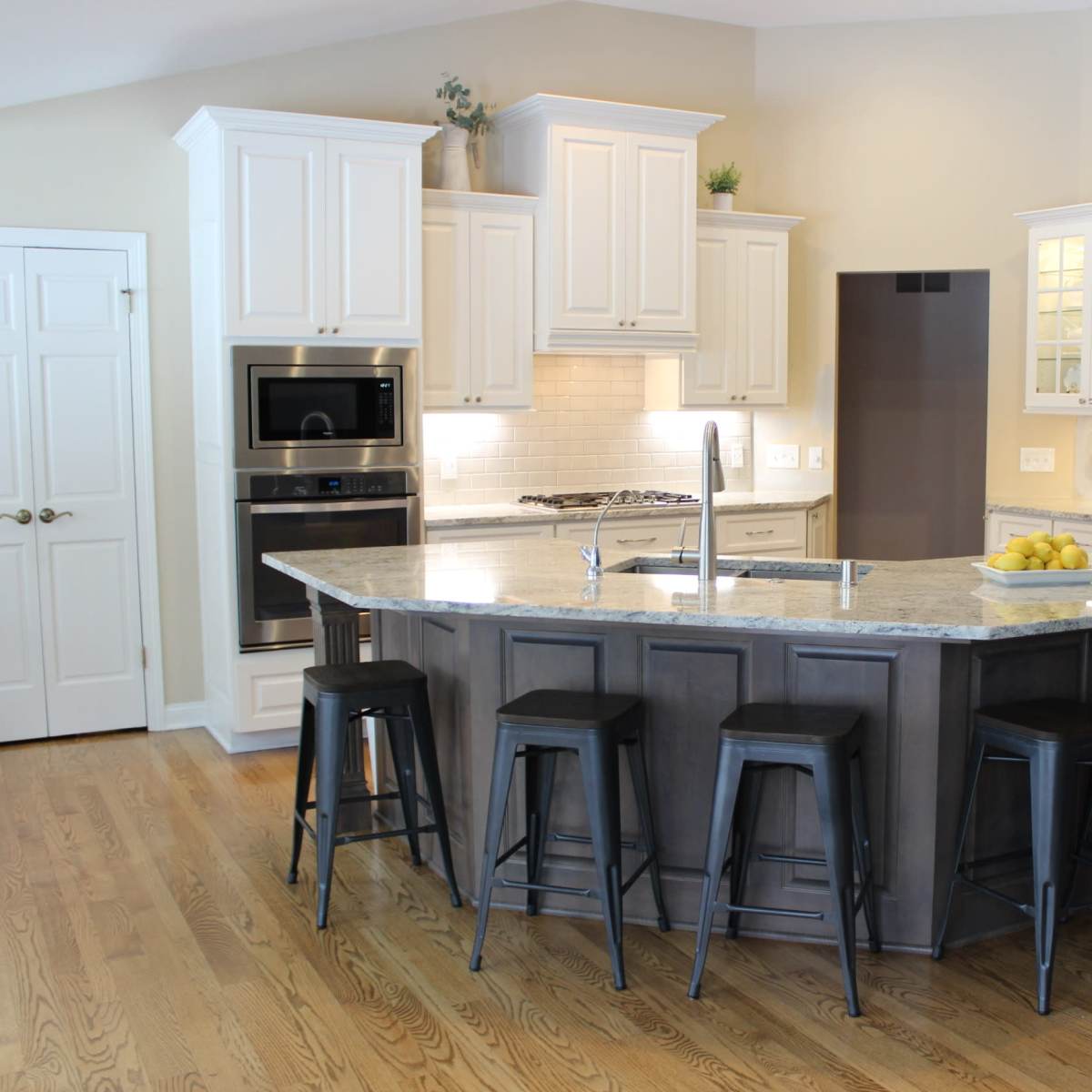 A modern kitchen with white cabinets, a central island with bar stools, and stainless steel appliances.