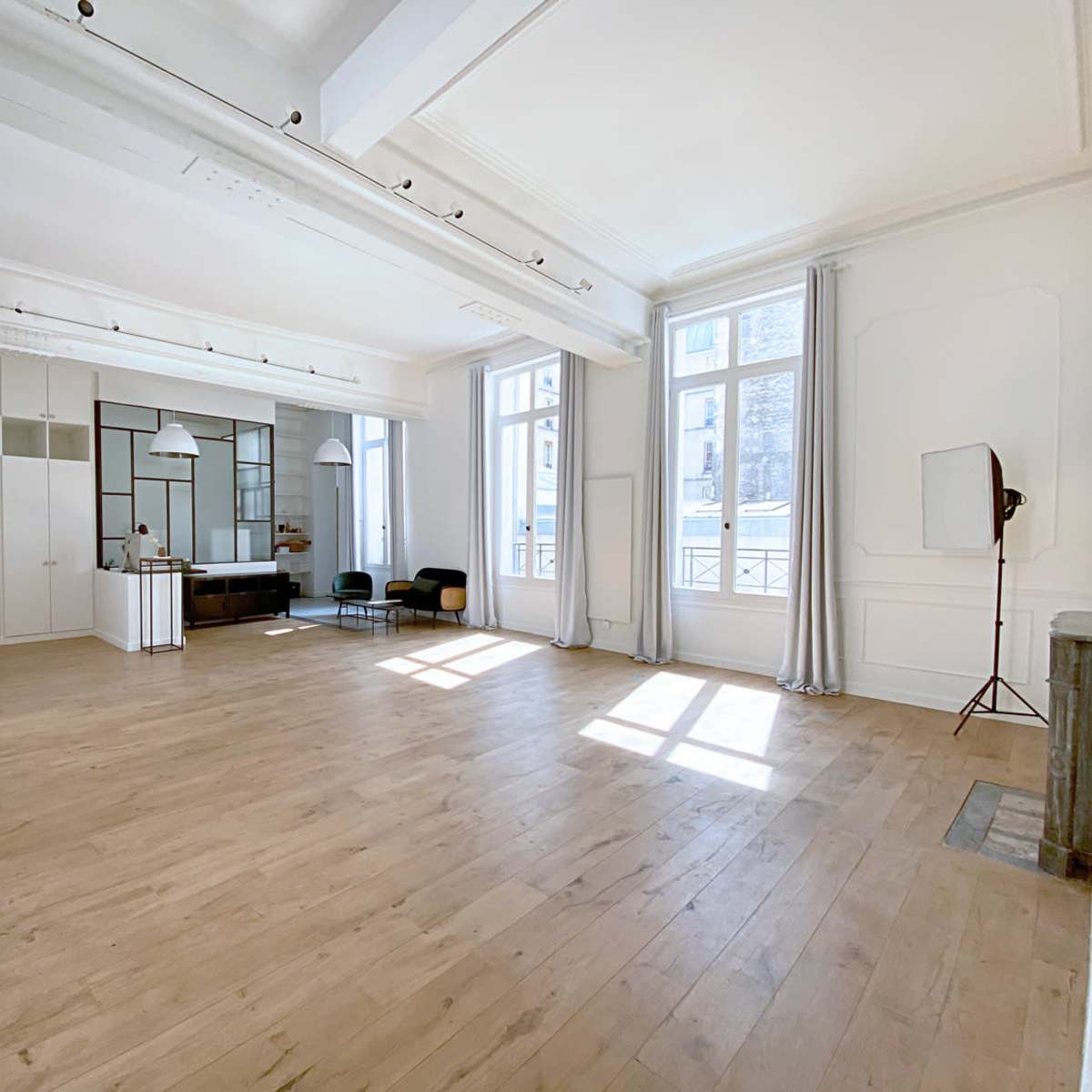A spacious, well-lit room with wooden flooring, large windows, and minimal furnishings.