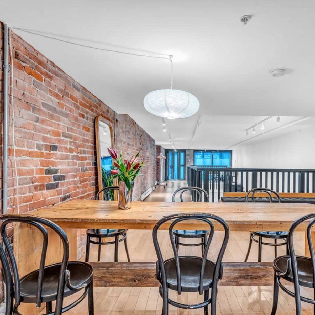 A spacious interior with exposed brick walls, a wooden dining table surrounded by black chairs, and a pendant light hanging from the ceiling.