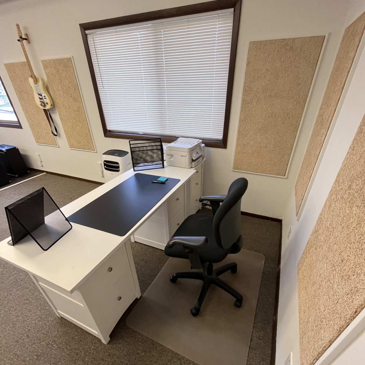 A small office space featuring a white desk with a black tabletop, a rolling chair, and a computer monitor, with soundproof panels on the walls.