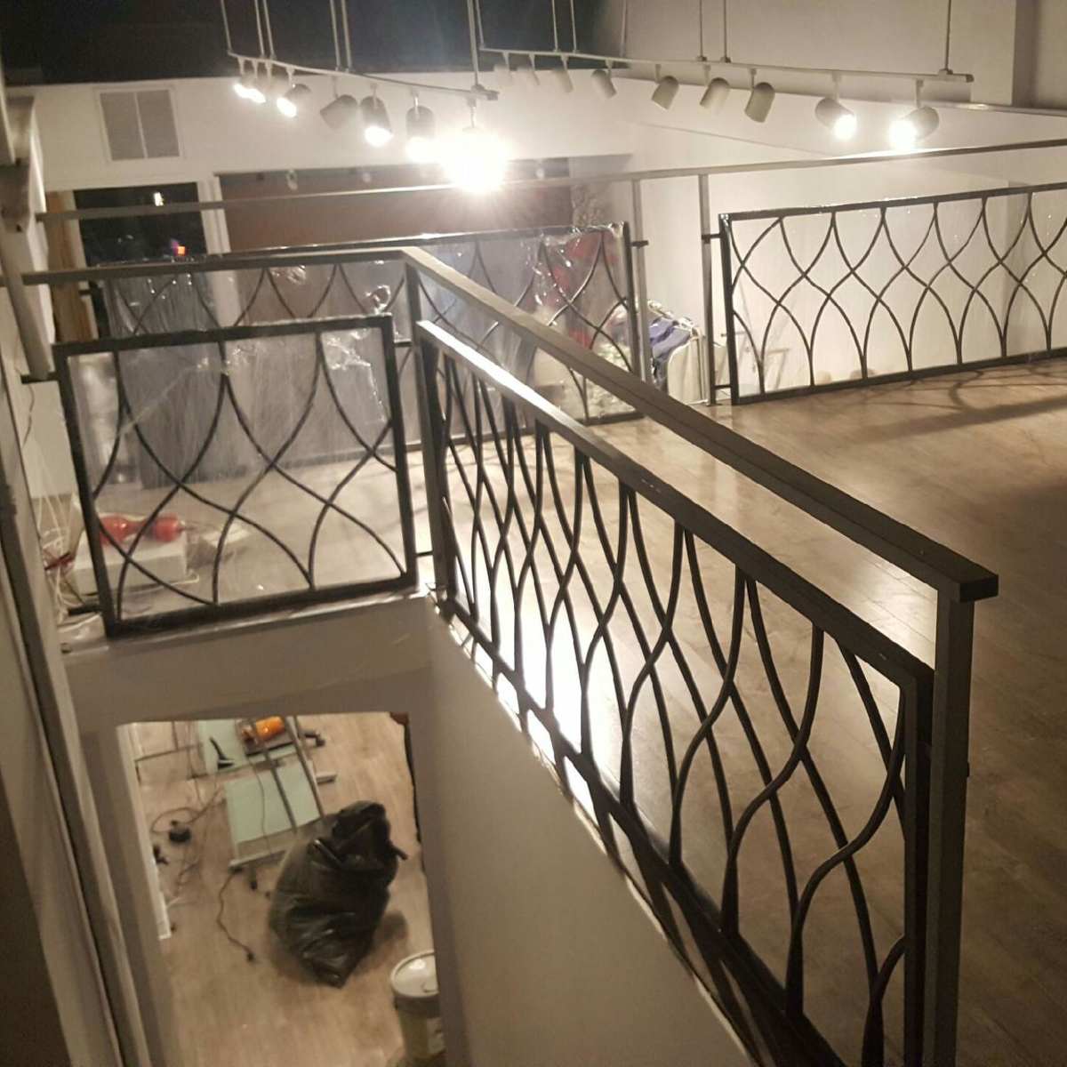 A spacious room with a wooden floor and a balcony railing overlooking the lower level, illuminated by overhead lights.