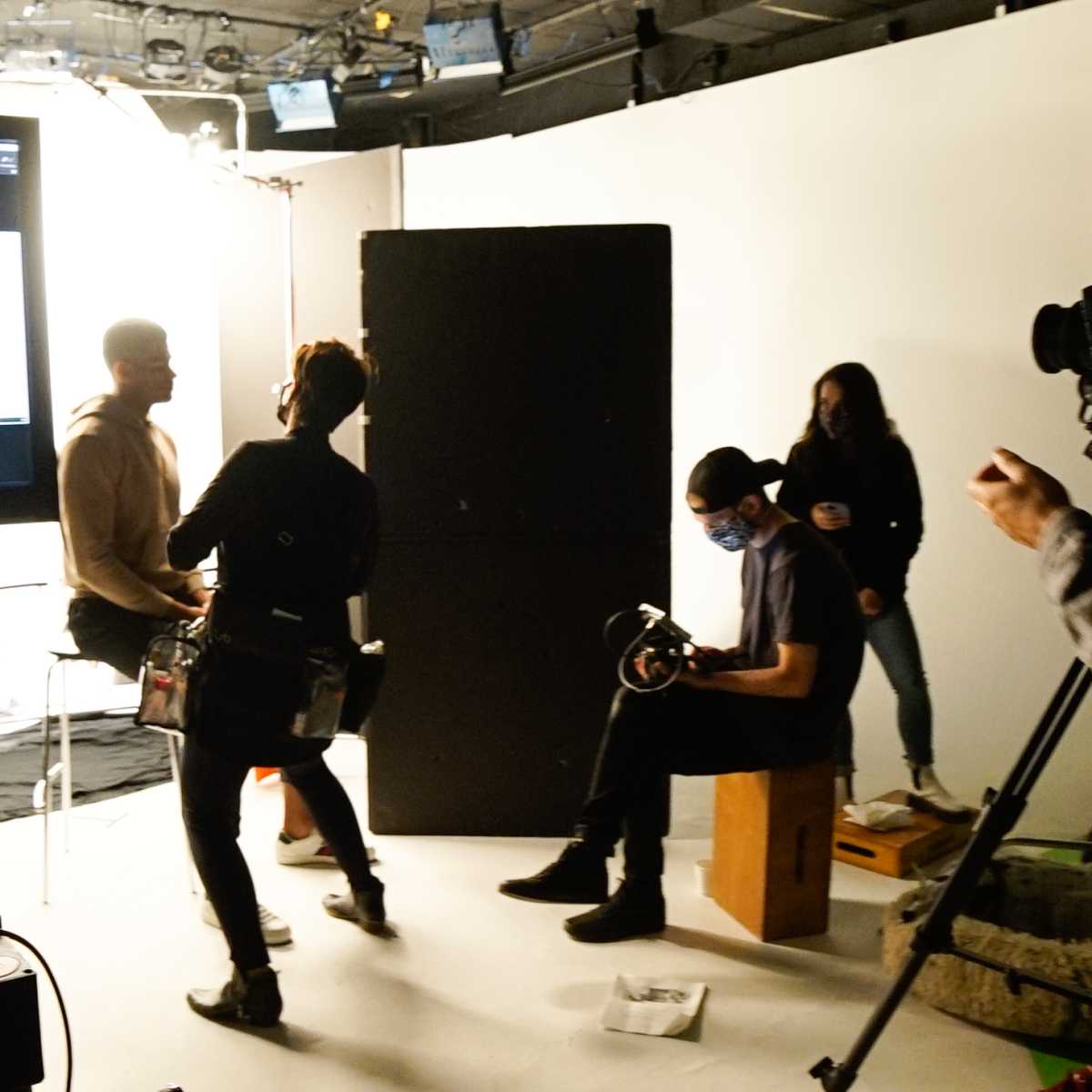 A film crew is preparing for a shoot in a studio, with several people working around a large monitor displaying silhouettes.
