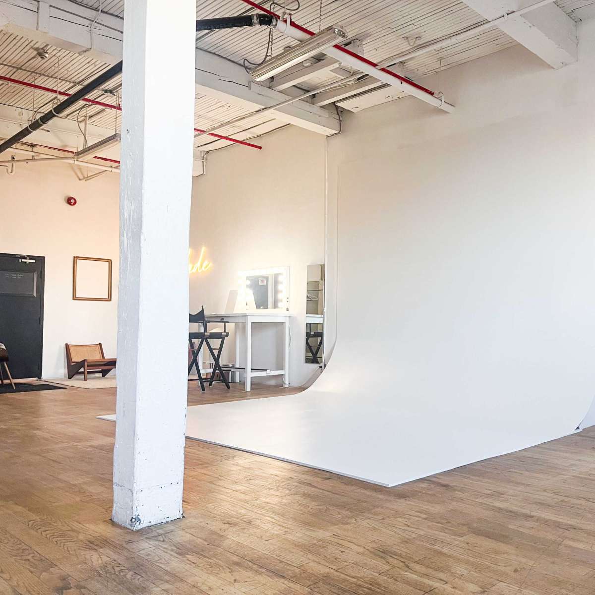 A spacious studio with a curved white backdrop, a mirror and table, and a colorful curtain arrangement on one side.