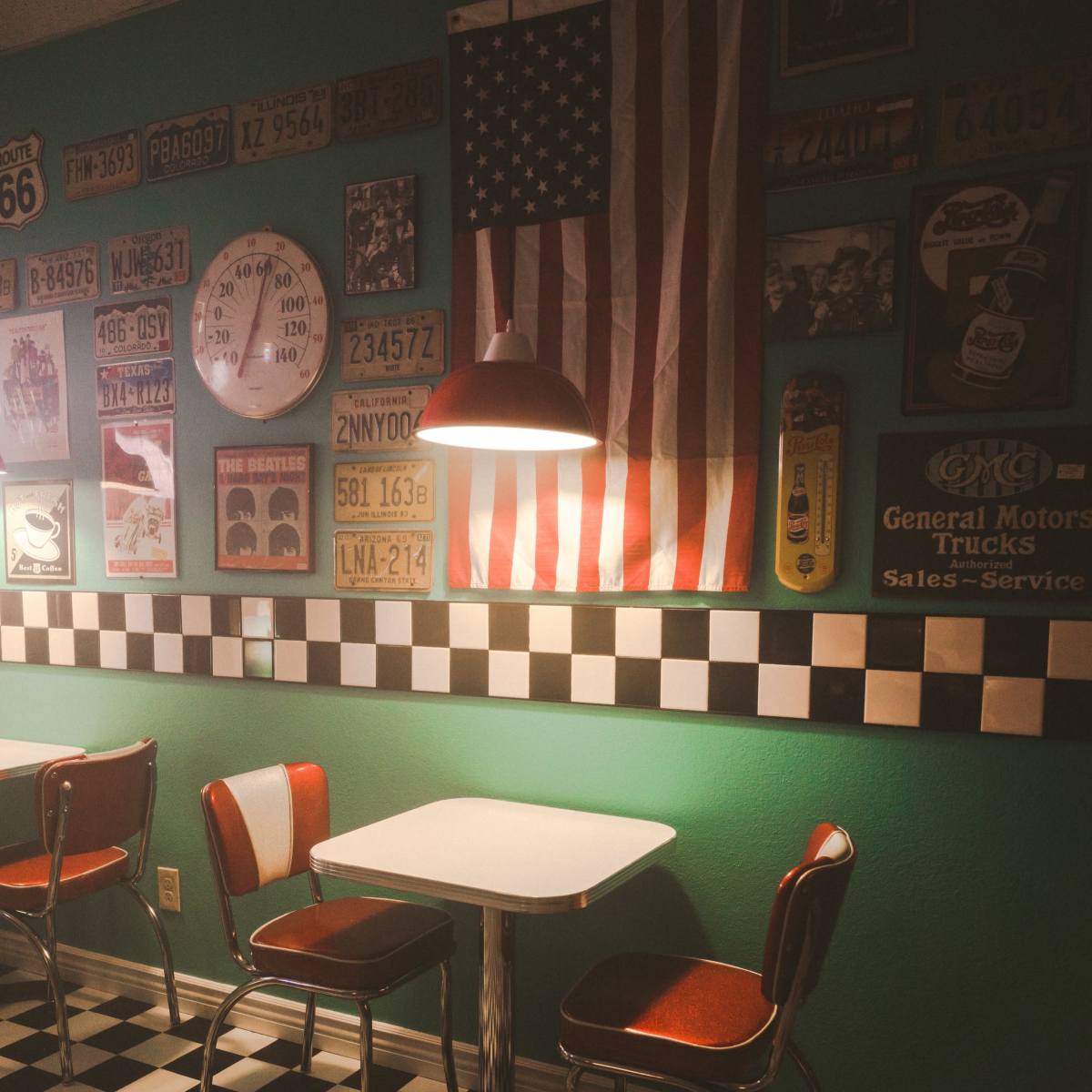A small diner corner features a checkerboard floor, a round table with metal chairs, and vintage American memorabilia on the walls, including an American flag.