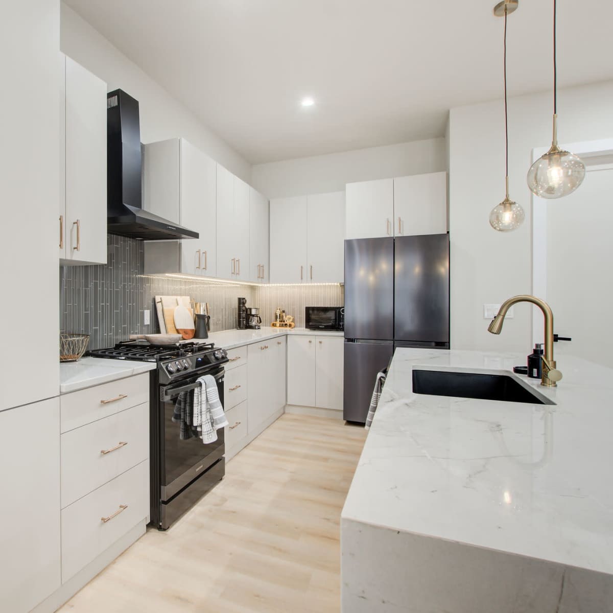 A modern kitchen features white cabinetry, a black stove, and a marble countertop with pendant lights overhead.