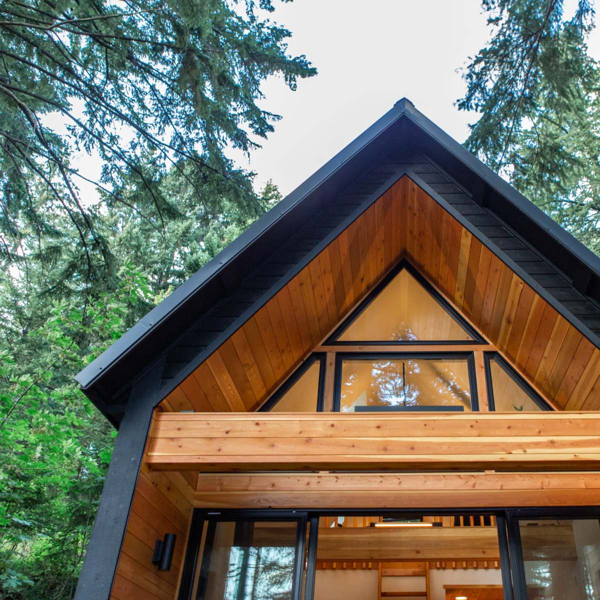 The exterior view of a wooden cabin with a triangular roof, framed by tall trees.