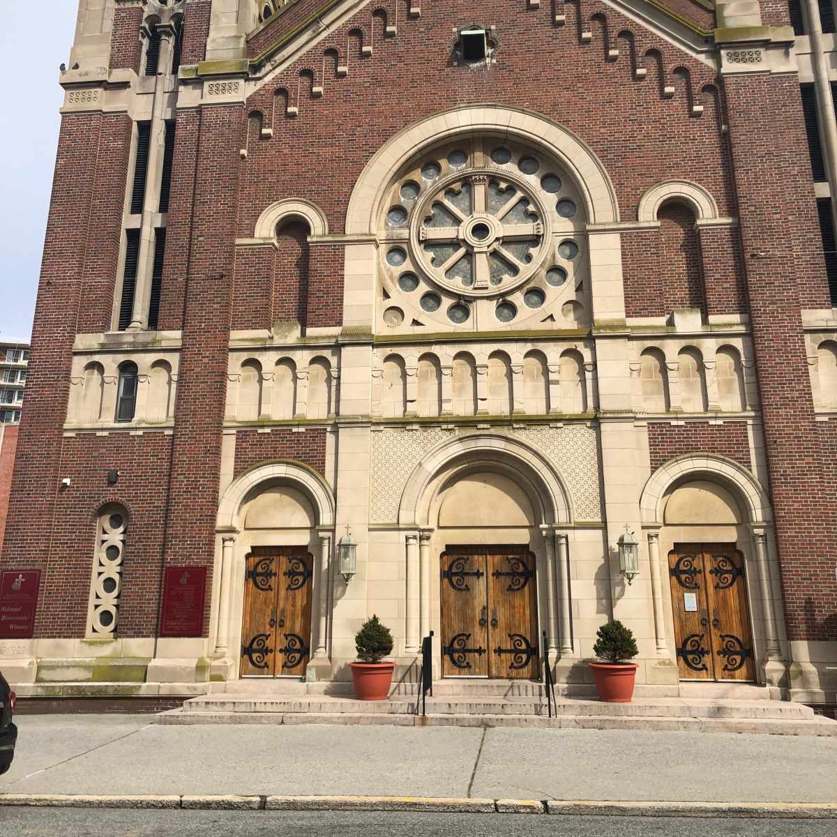 A brick church with two tall spires, a large rose window, and wooden double doors at the entrance.