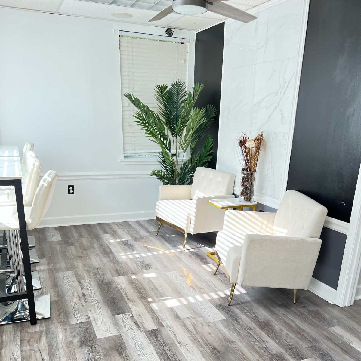 A modern room with two white chairs and a small table near a palm plant, set on light wood flooring.