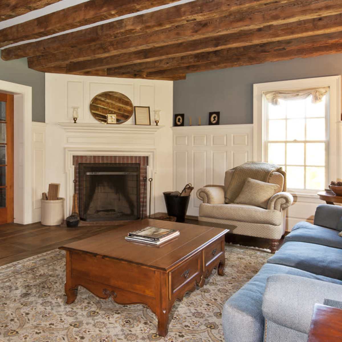 The living room features exposed wooden beams, a fireplace with a brick surround, a wooden coffee table, and a comfortable seating arrangement.