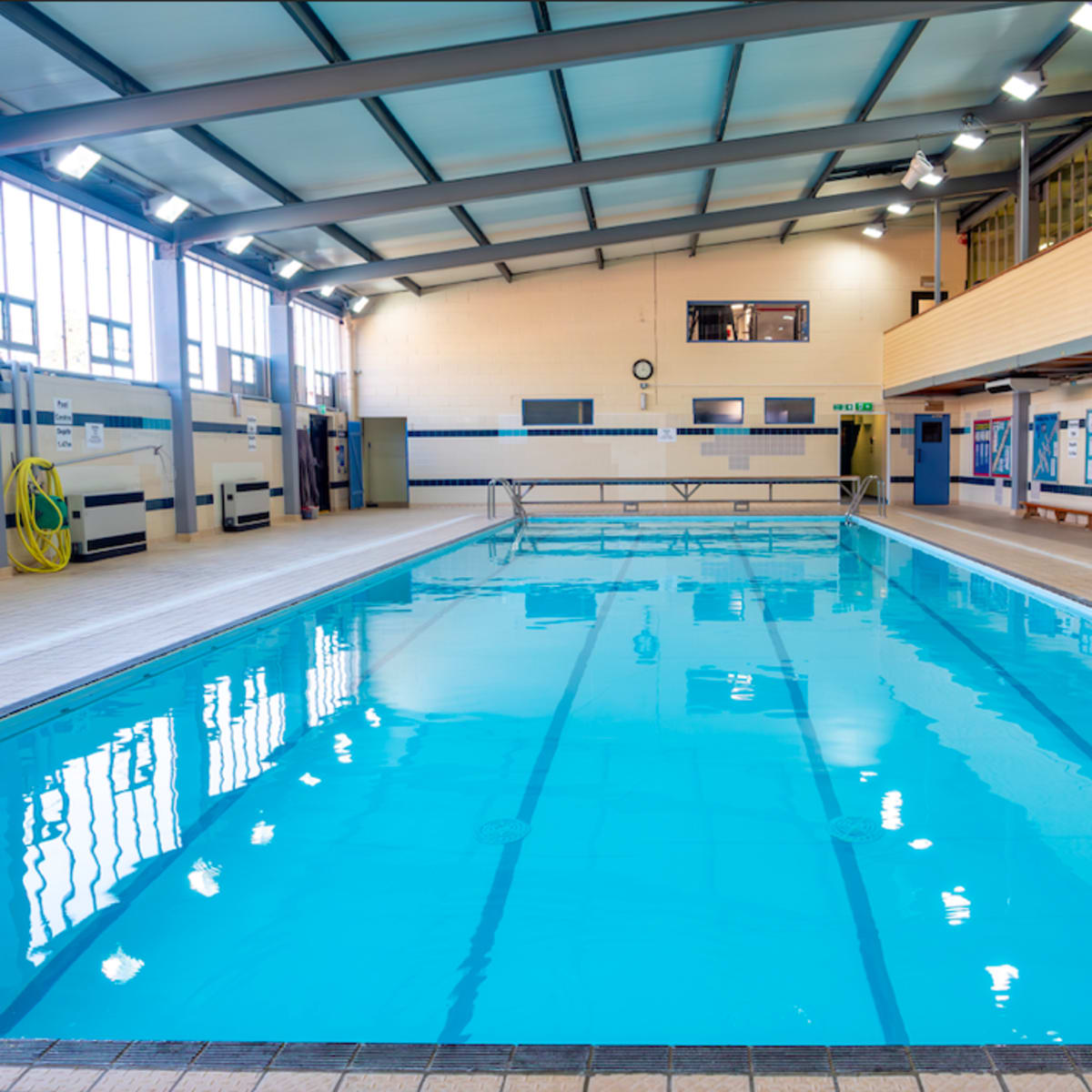 A well-lit indoor swimming pool with clear blue water and a wooden deck area.