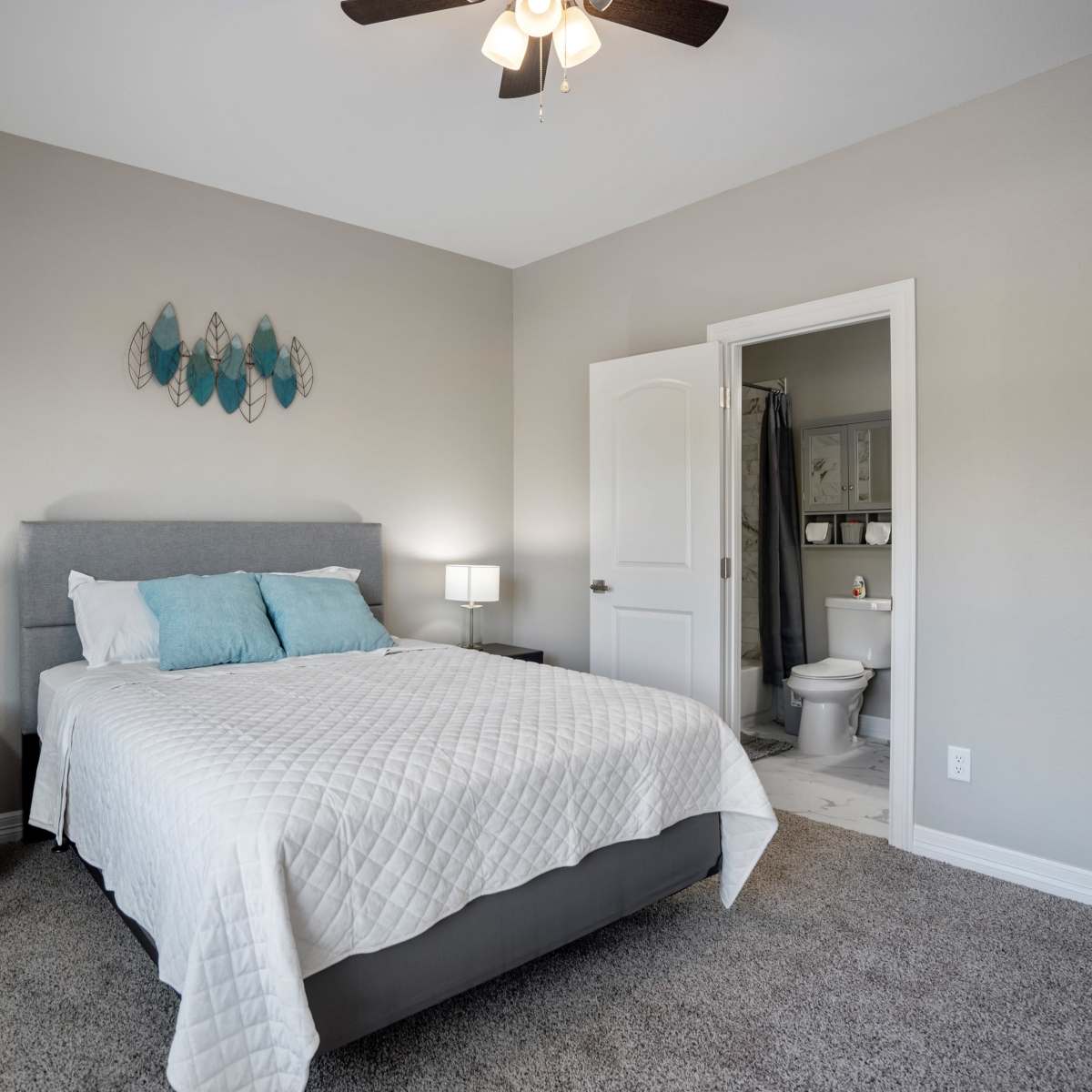 A neatly arranged bedroom with a bed, nightstands, and an open bathroom door in the background.