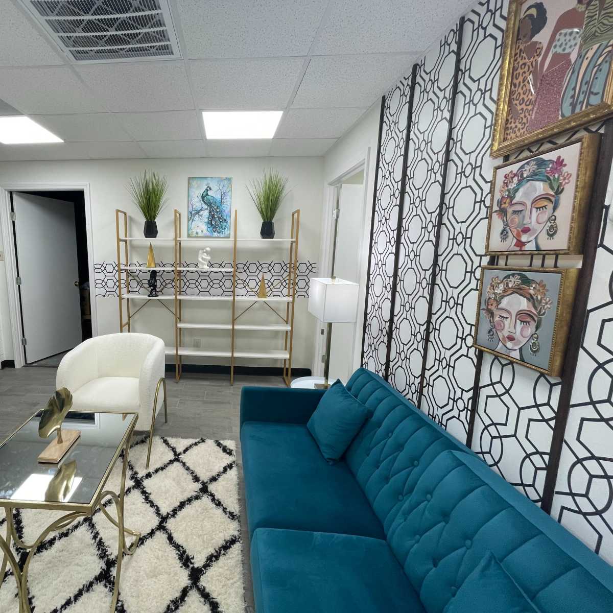 A modern office waiting area featuring a teal sofa, two white armchairs, a glass coffee table, and decorative wall art.