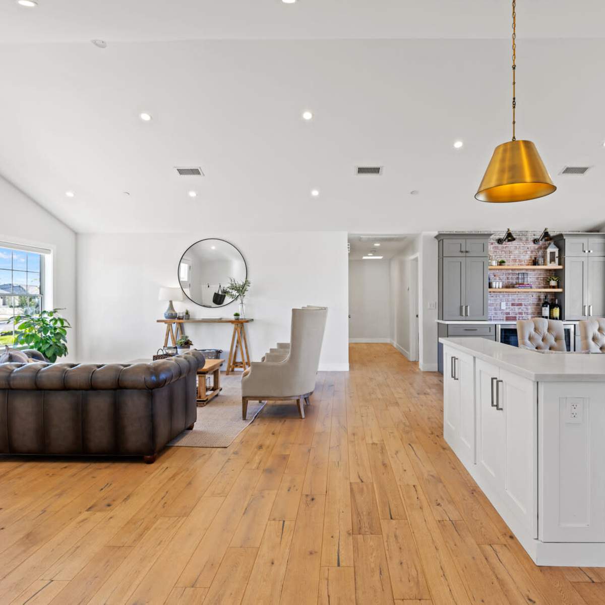 A spacious, modern living area with a sectional couch, a dining table, and a kitchen featuring white cabinets and a stainless-steel refrigerator.