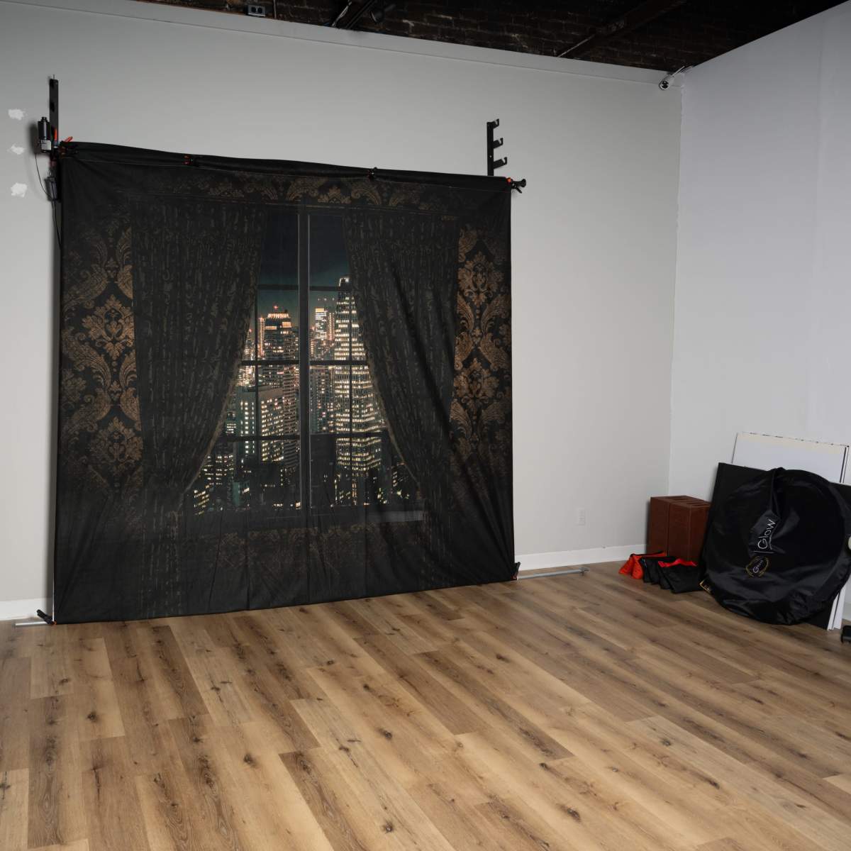 A photography studio features a dark backdrop with a window scene overlooking a city skyline, set against a wooden floor.