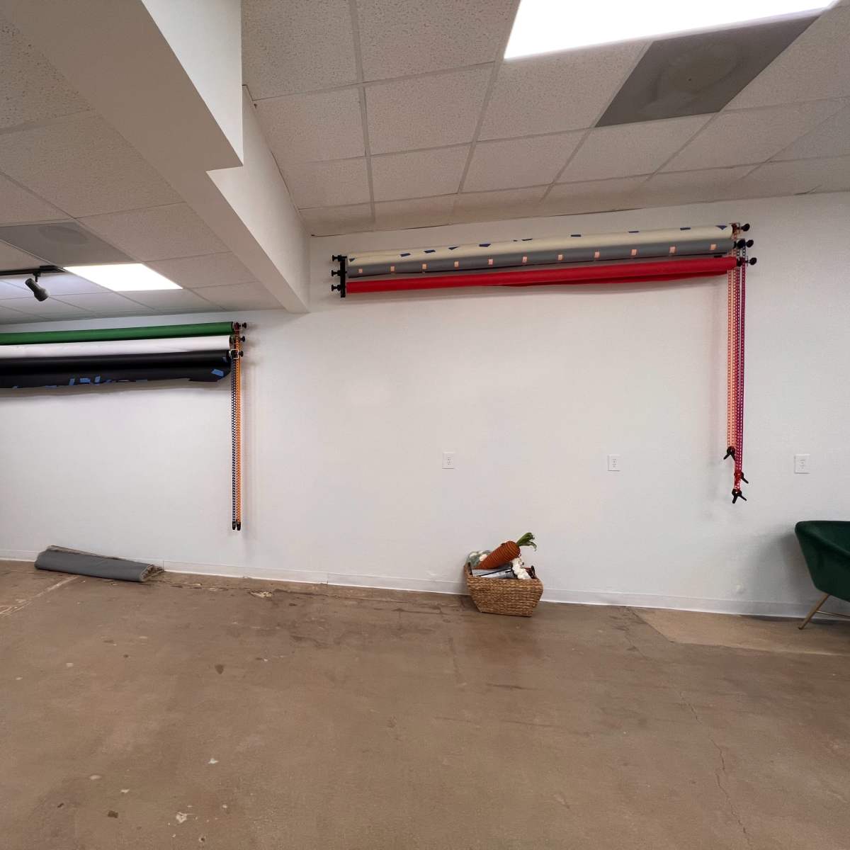 A minimalist studio space with various colored backdrops hanging on the wall and a few decorative items on the floor.