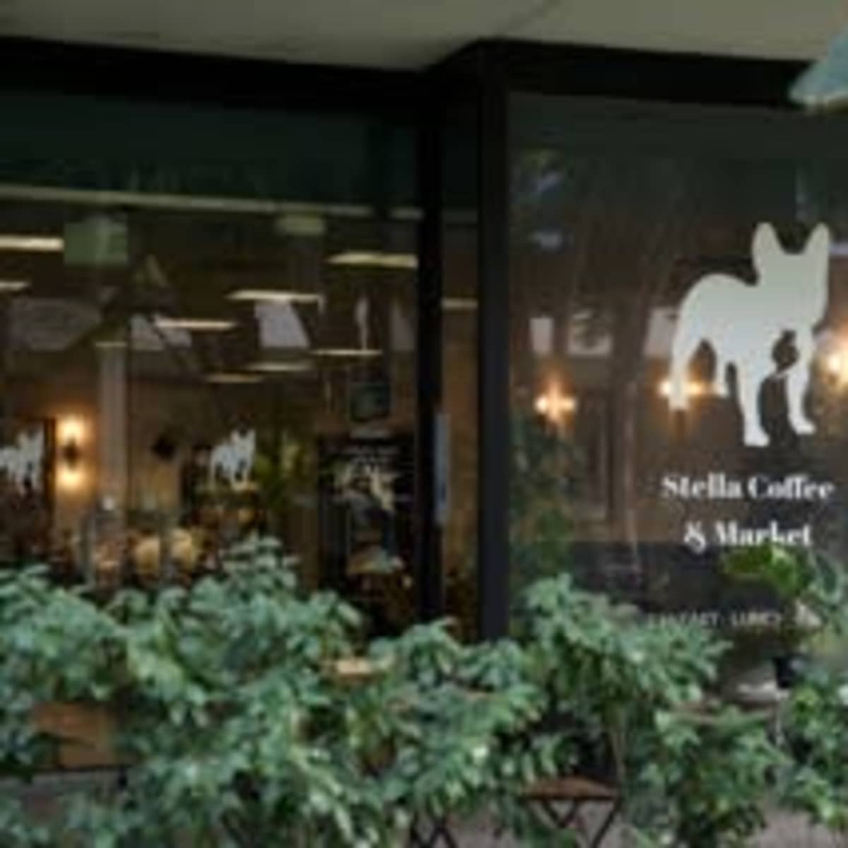 A storefront featuring "Stella Coffee & Market," with a silhouette of a dog in the window and outdoor seating in front.