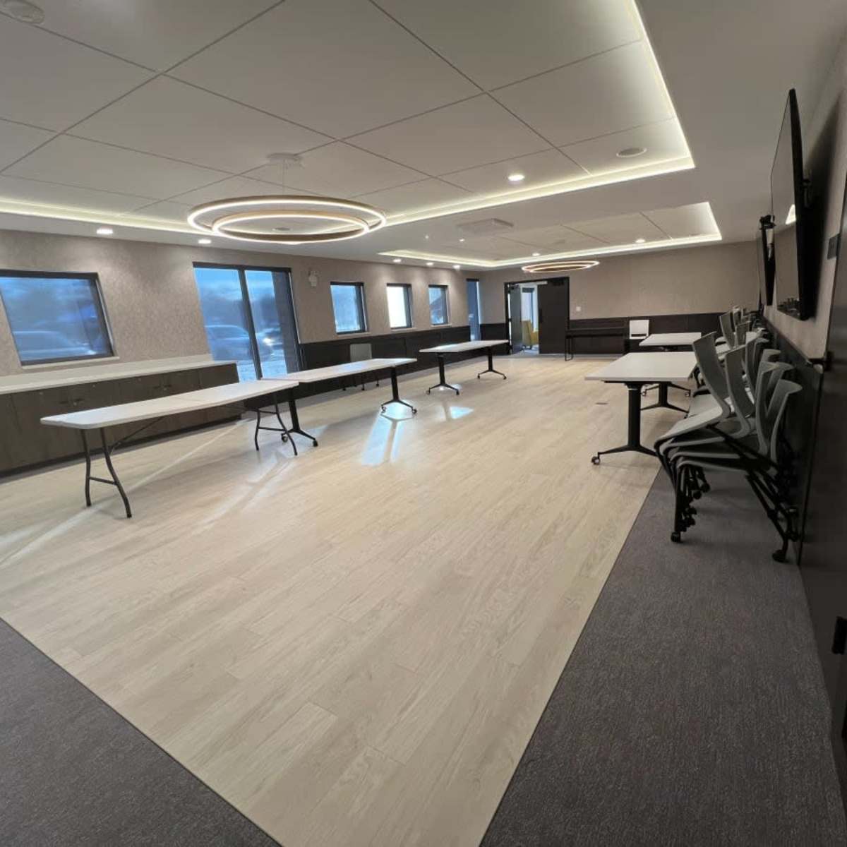 A spacious meeting room with several tables arranged in the center and chairs stacked against the wall.