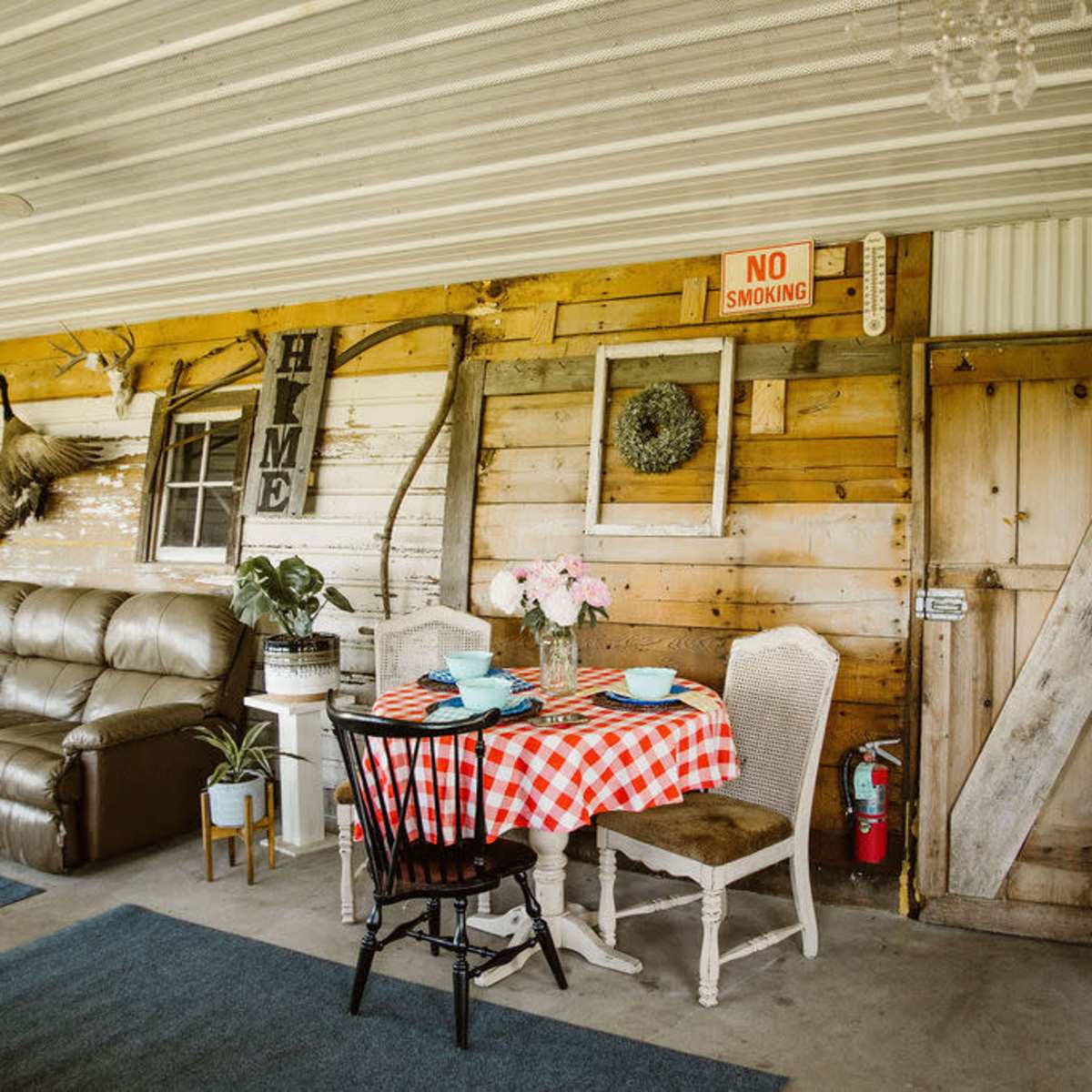 A rustic interior featuring a checkered tablecloth on a small dining table, a leather couch, and wooden walls with decorative elements.