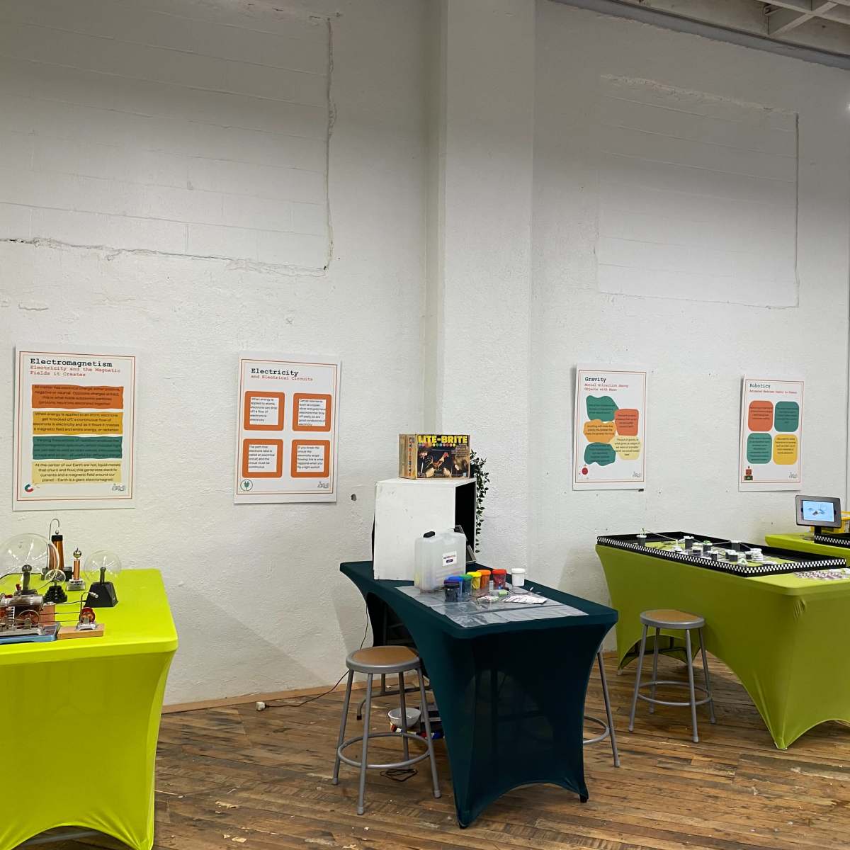 A spacious room with two distinct tables covered in colored cloths, displaying various scientific equipment and signage on the walls.
