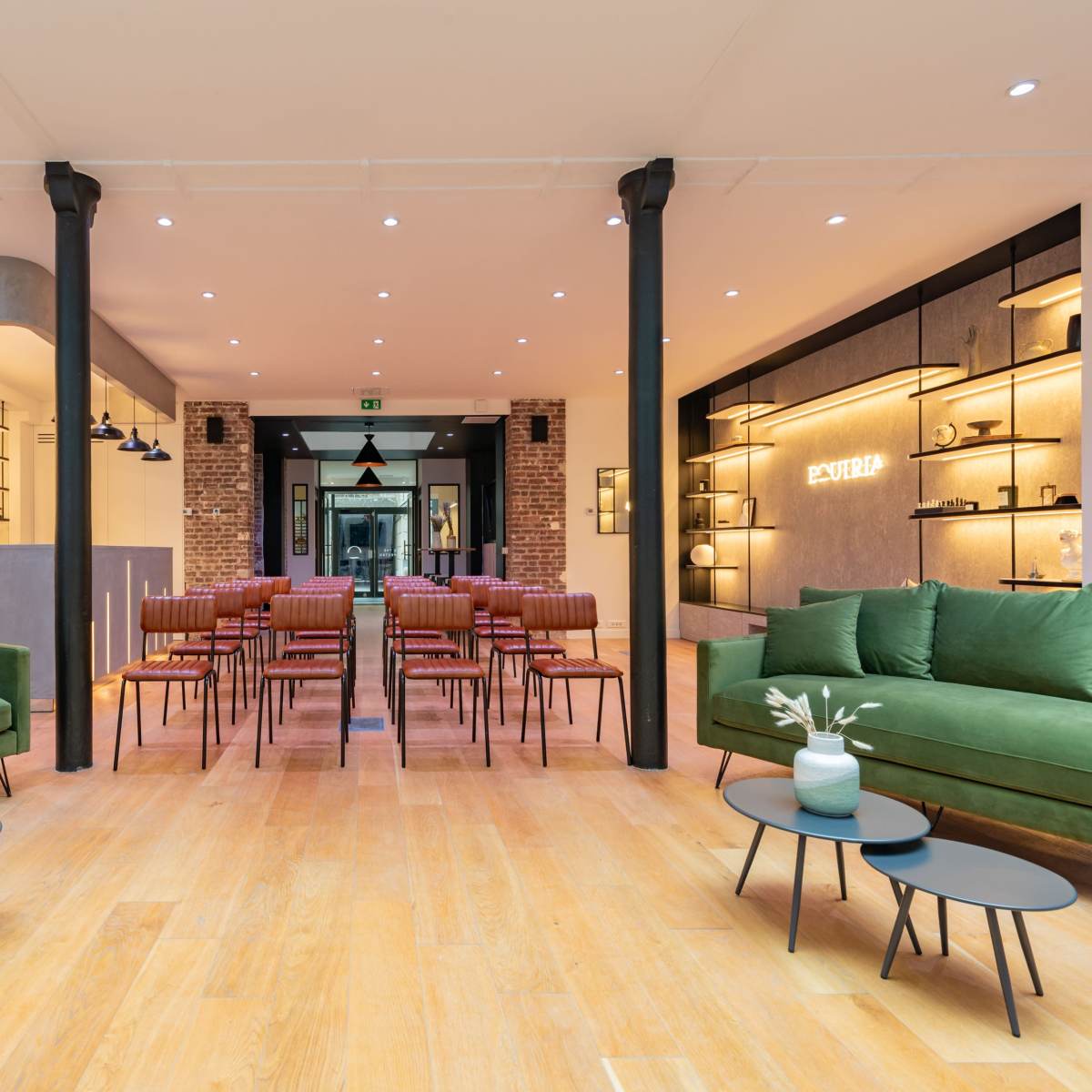 A modern interior space with green sofas, small tables, and rows of chairs arranged for an event.