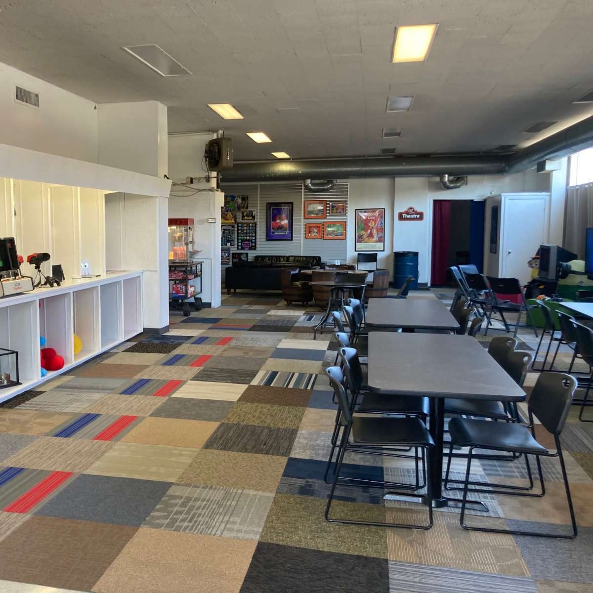 A spacious game room with white shelving displaying various games on one side and rows of tables and chairs arranged neatly on the other side.