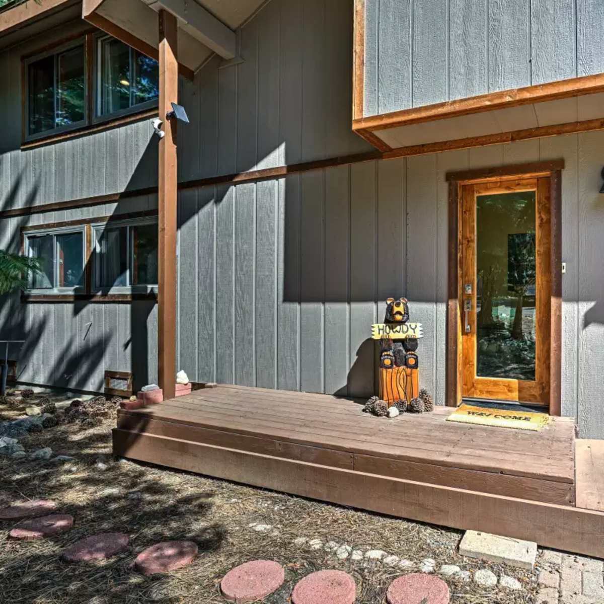A welcoming entrance with a wooden deck and a sign next to the front door of a house that features gray siding.