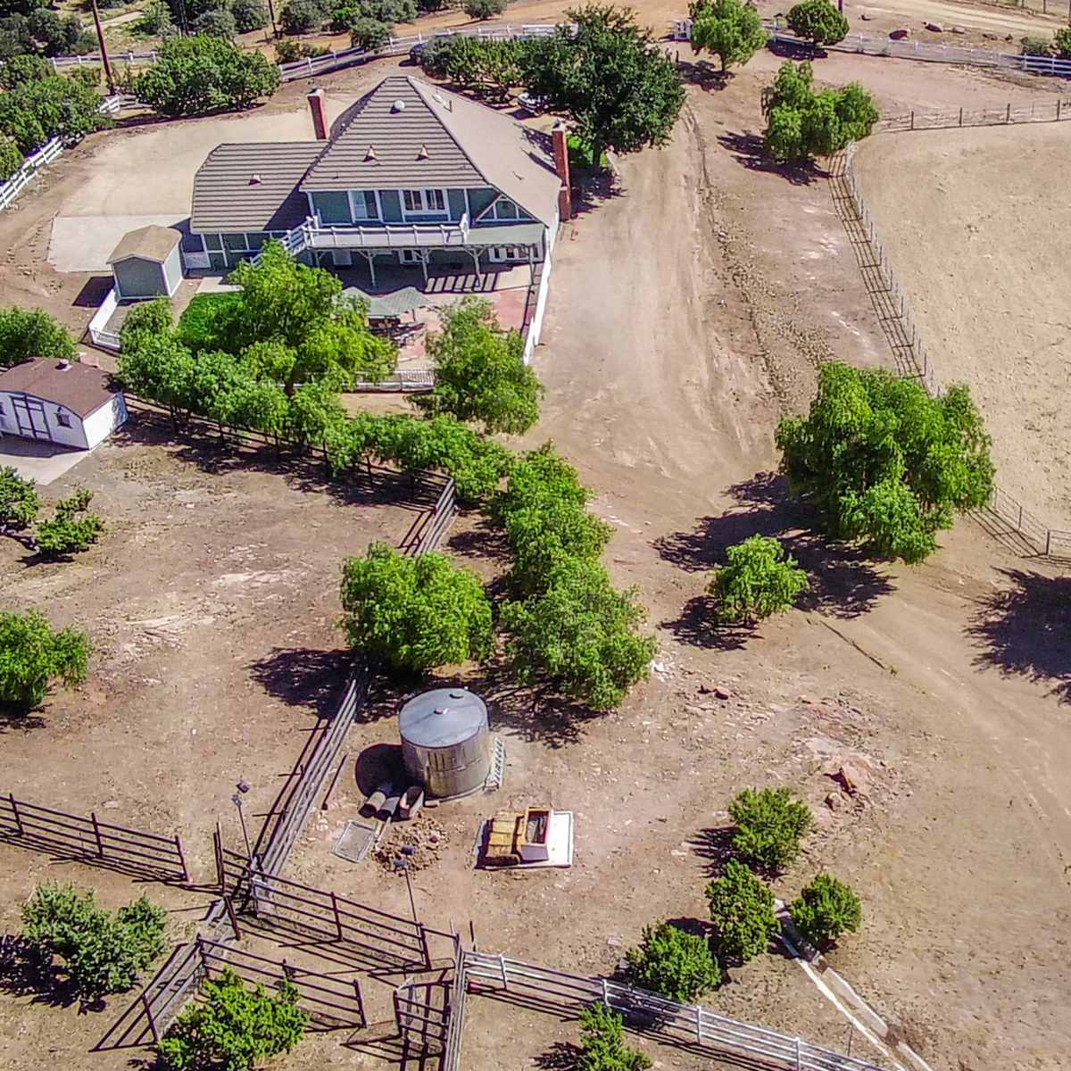 An aerial view of a rural property featuring a large house, a fenced area, trees, and sparse land.
