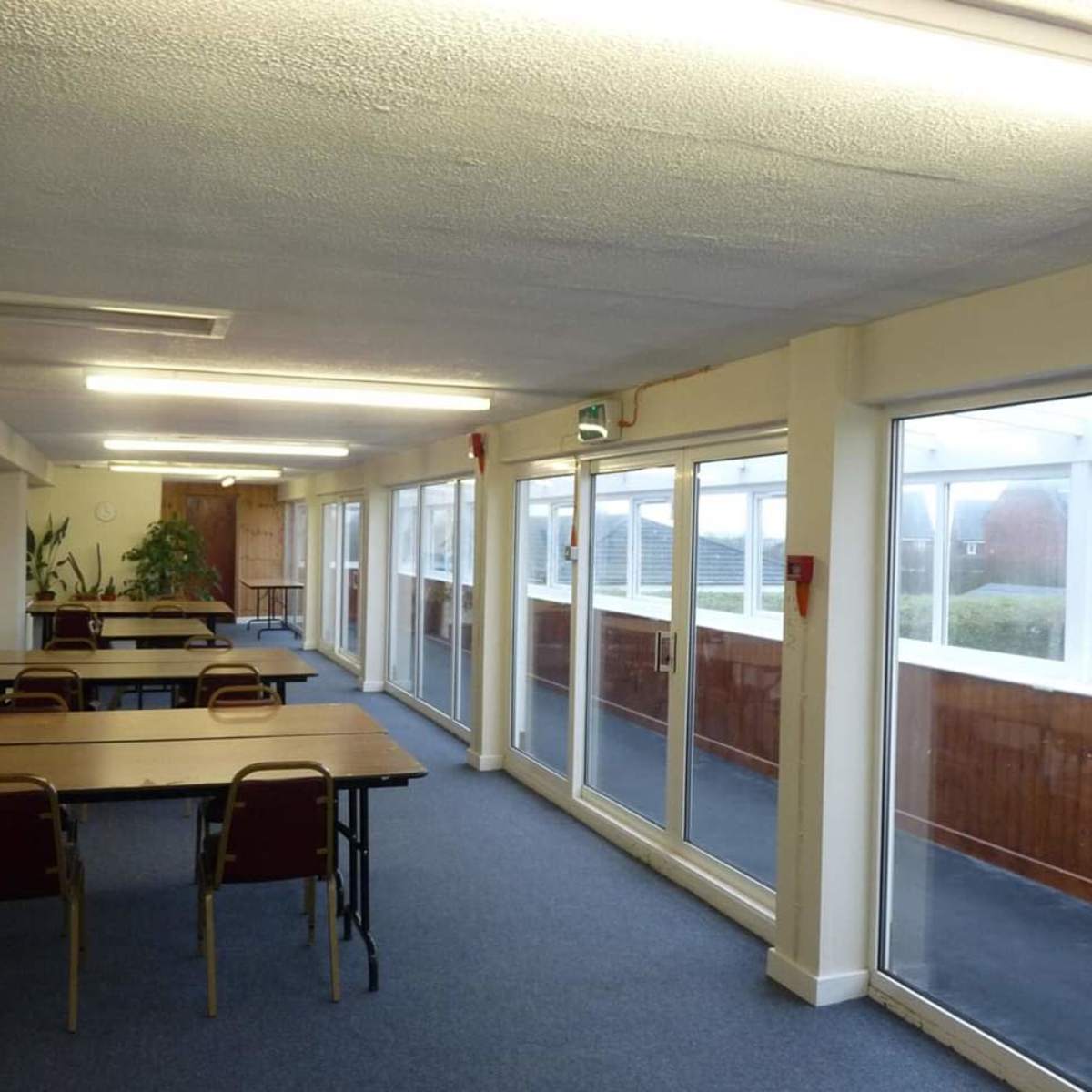 A long interior hallway with several tables and chairs set up, featuring large glass doors that open to an outdoor area.