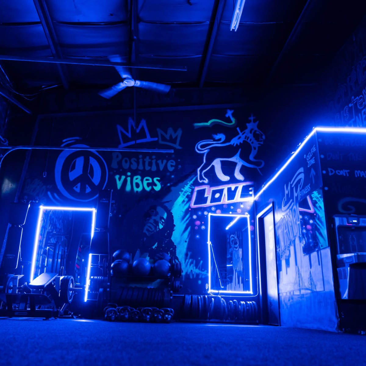 A vibrant gym interior with neon blue lighting, motivational murals on the walls, and exercise equipment visible on the floor.