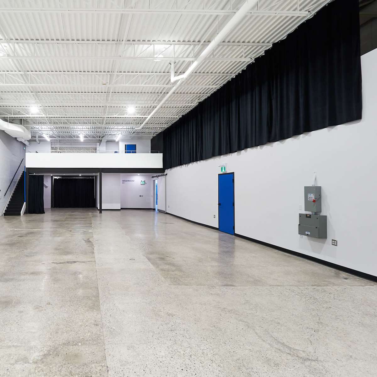 A spacious, empty hall with a polished concrete floor, white walls, and black drapes at one end.