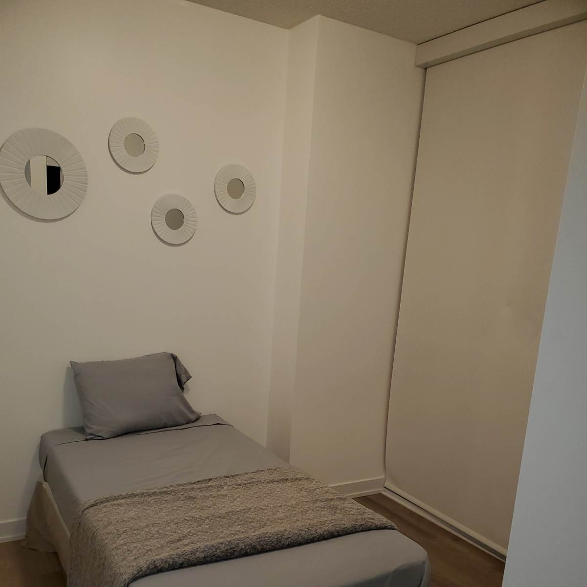 A small bedroom with a single bed, a gray blanket, and circular wall decor.