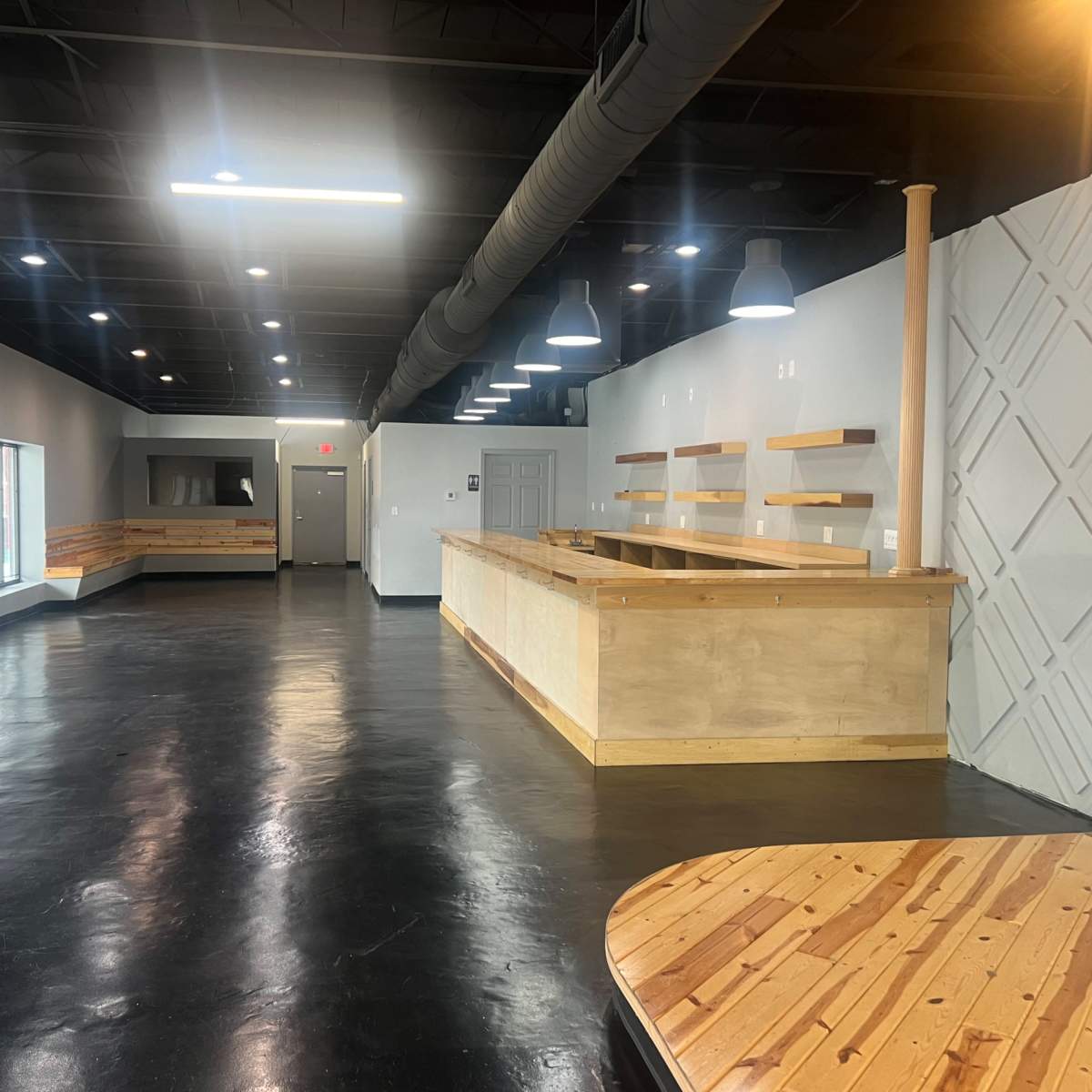 A spacious, modern interior with a wooden reception counter and benches along the walls, featuring a polished black floor and overhead lighting.