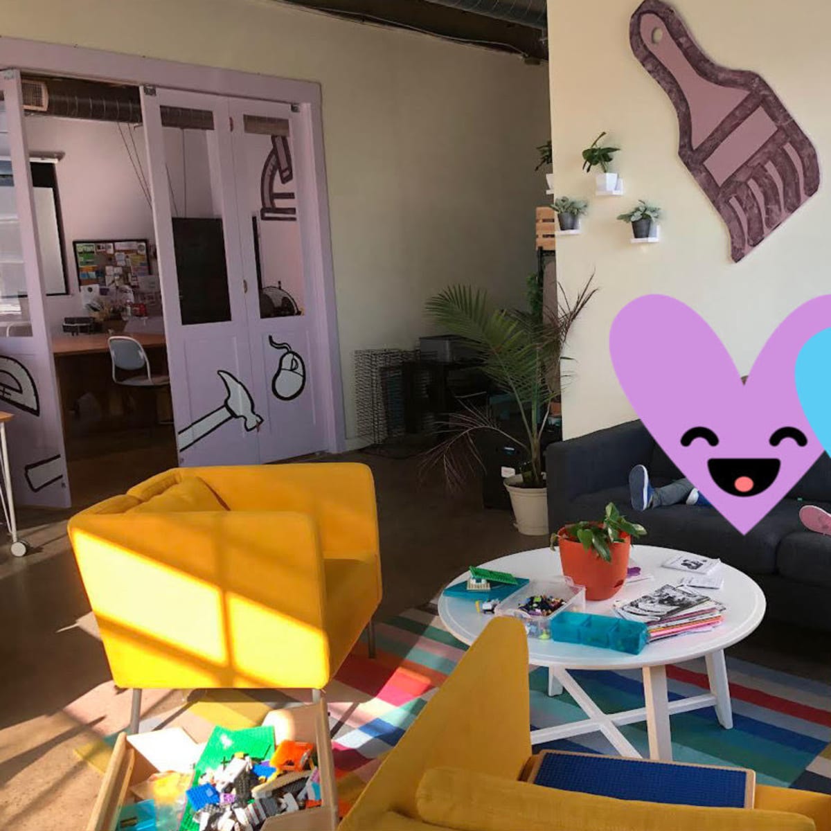 A brightly colored lounge area features a sofa, two armchairs, a coffee table with various items, and a doorway leading to another room.