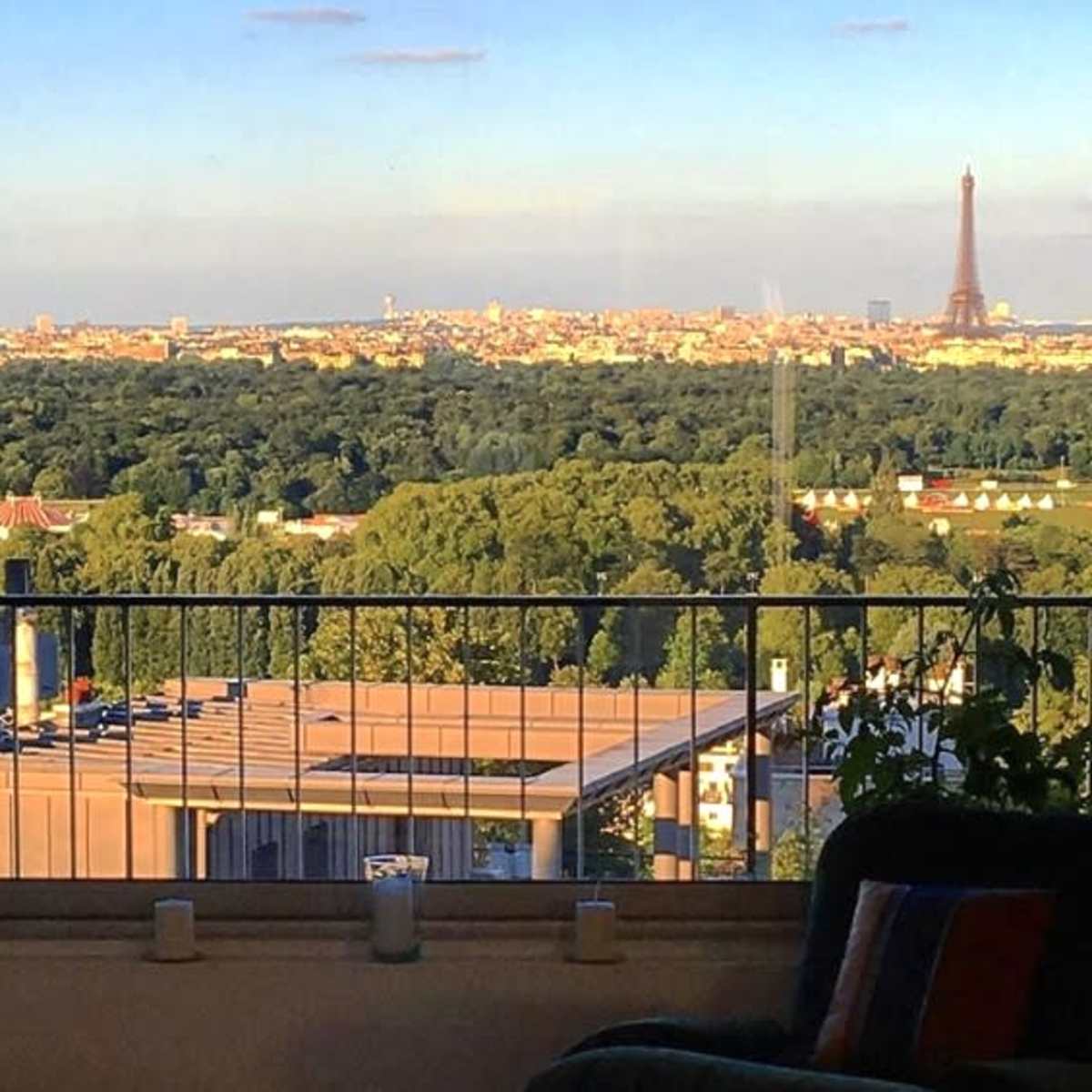 A view of the Eiffel Tower from a window overlooking a green landscape and city skyline.
