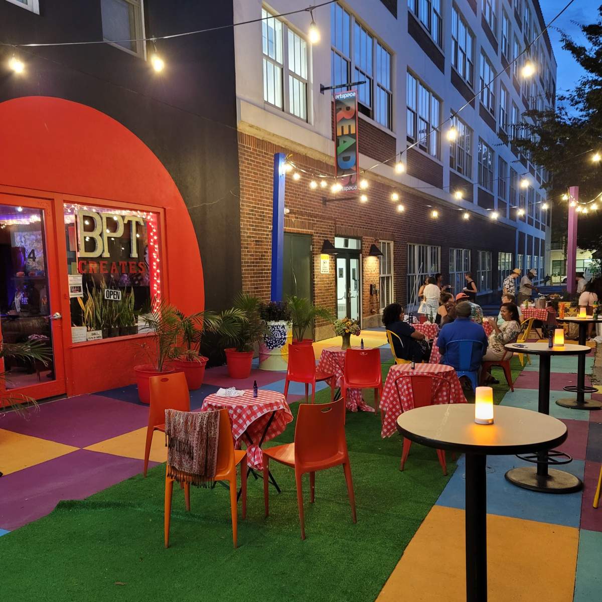 An outdoor dining area with colorful table settings and string lights in front of a restaurant.