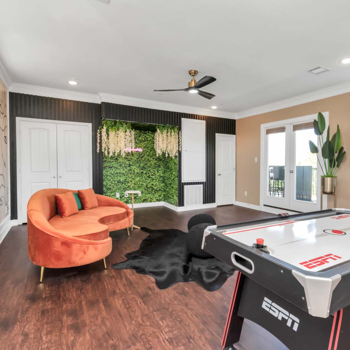 The room features a pool table, an orange sofa, and a wall adorned with greenery.