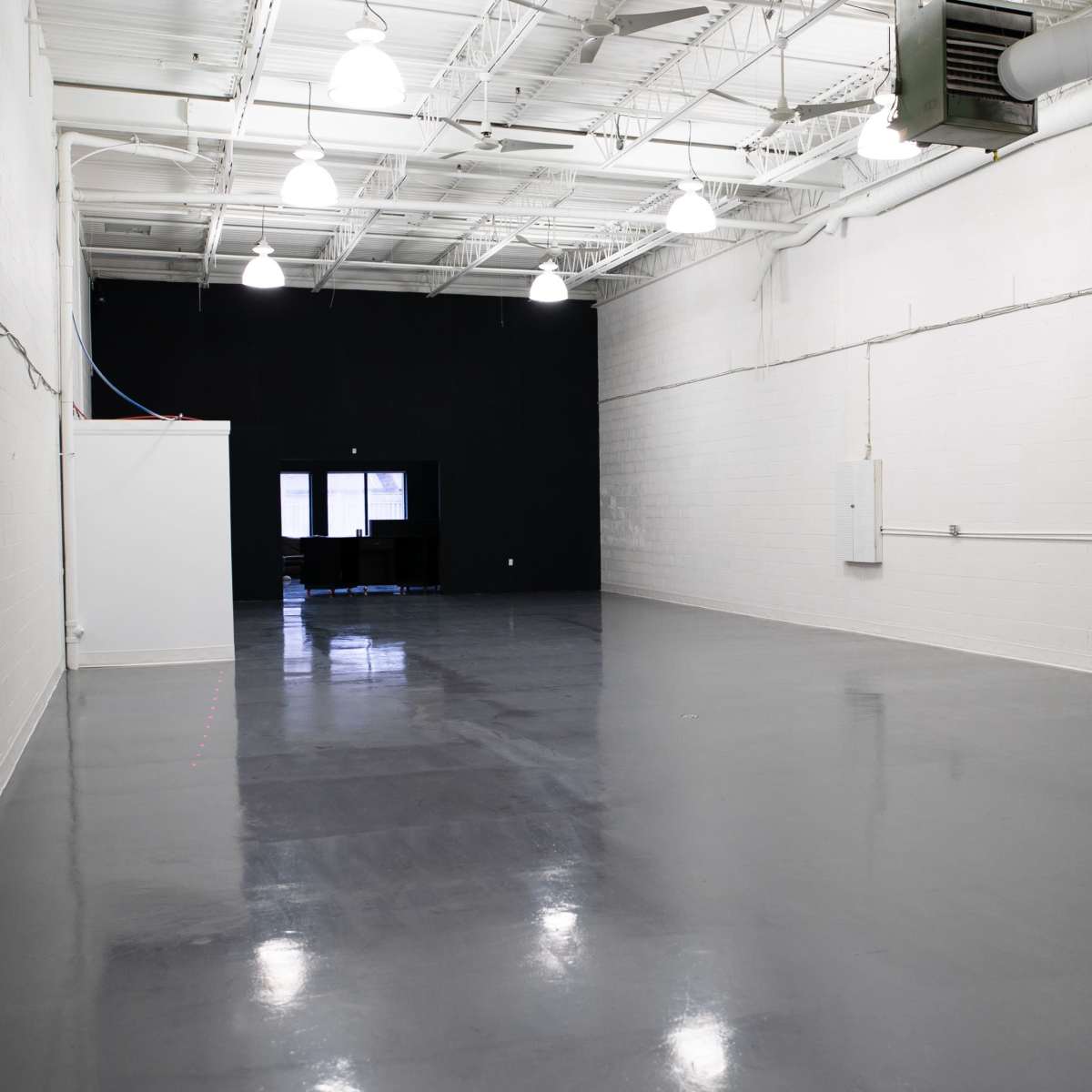 A large, empty indoor space with white walls, a polished gray floor, and a black wall at one end.