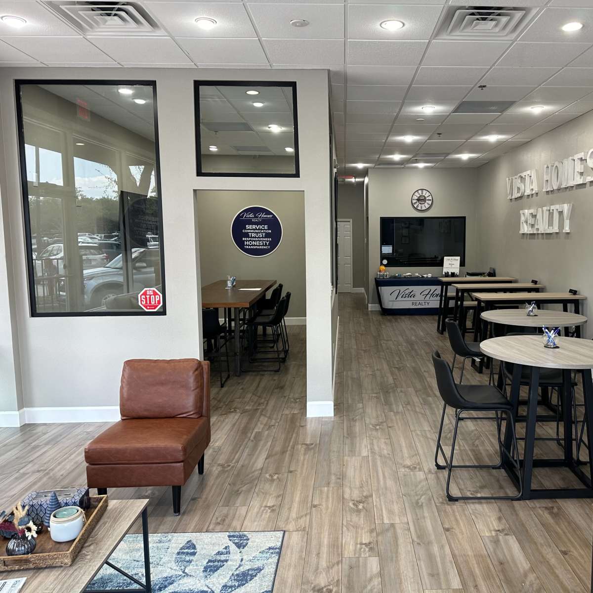 A modern real estate office with a reception area, several tables and chairs for meetings, and the company name prominently displayed on the wall.