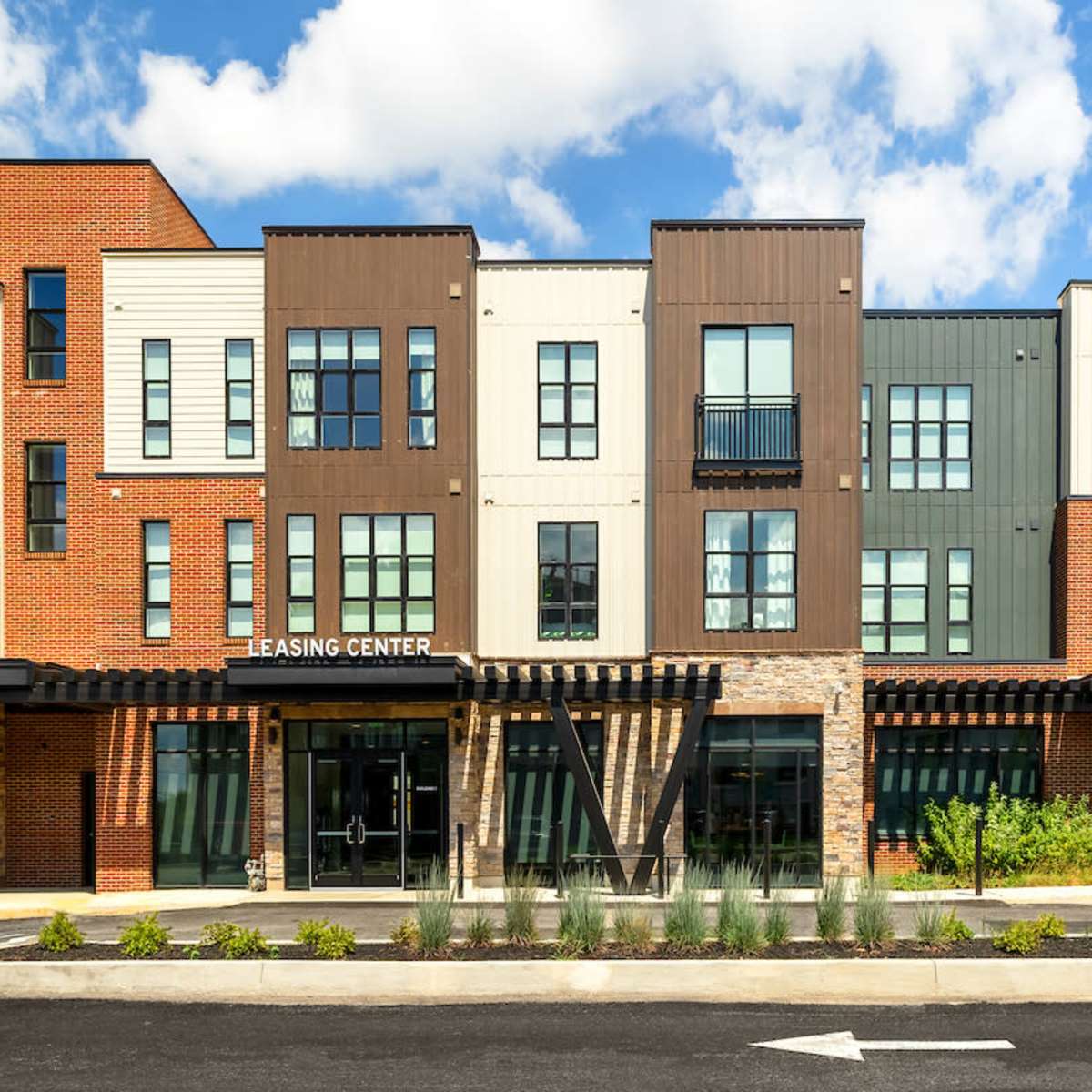 A modern leasing center building with a mix of brick and metal siding, featuring multiple windows and a covered entrance.