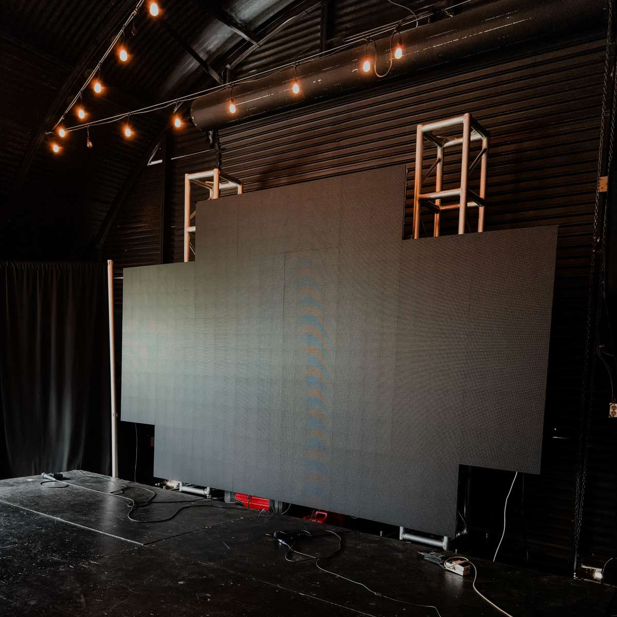 A large, blank display screen is mounted on a stage with studio lighting and power cables visible.