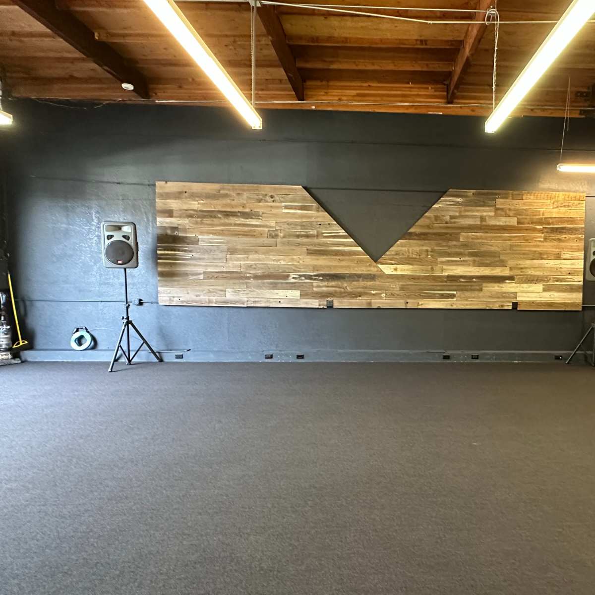 A spacious room with a wooden accent wall, two speakers on stands, and a wooden piano in the corner.