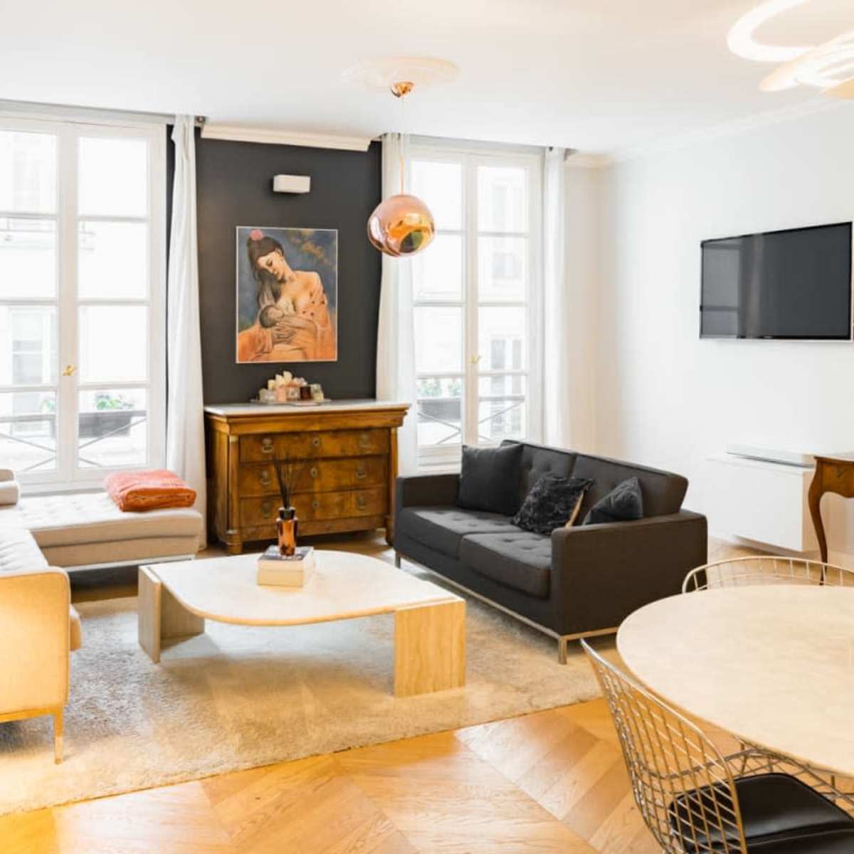 The living room features two sofas, a coffee table, a dining area with round table, and large windows letting in natural light.