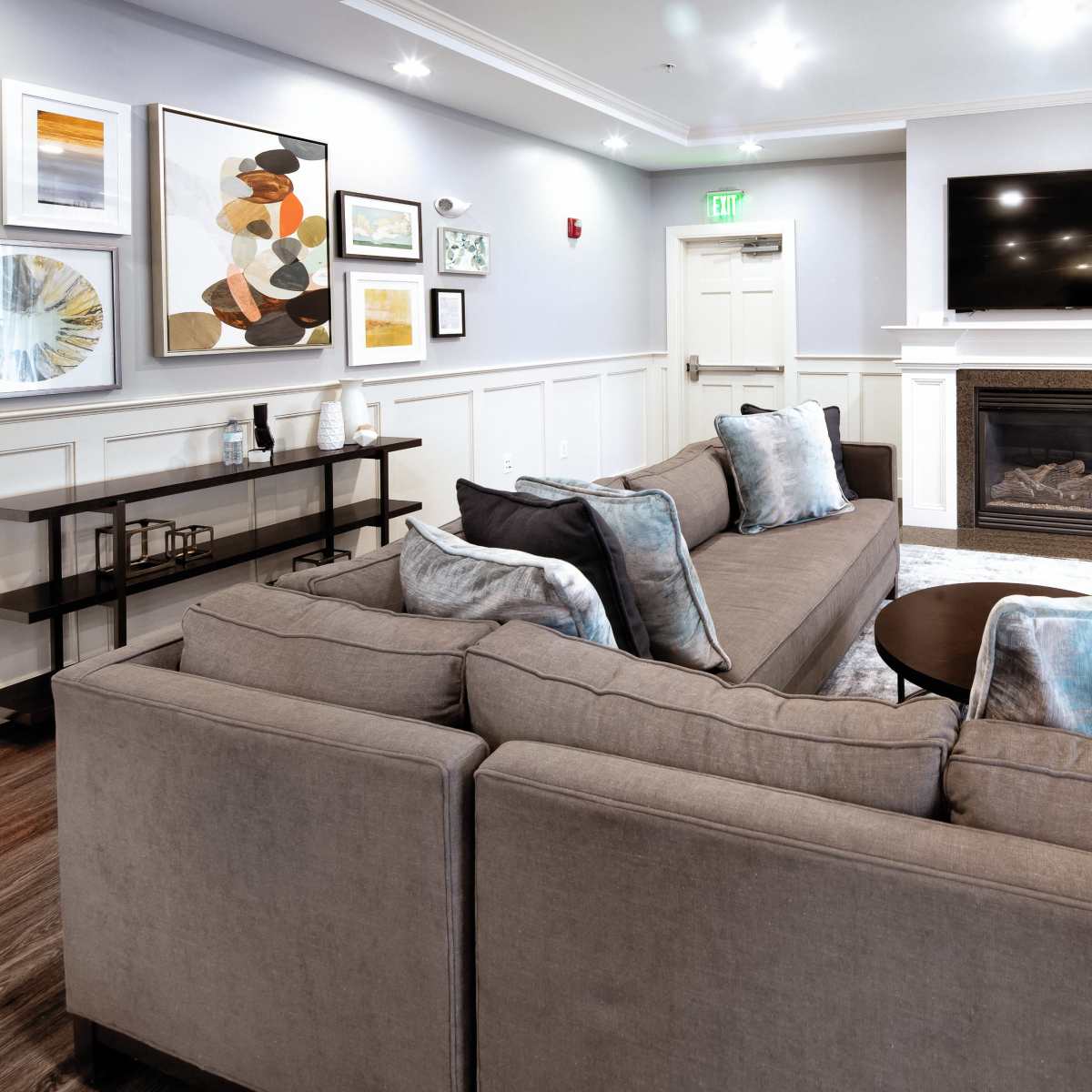 A modern living room with a sectional sofa, a coffee table, a fireplace, and a wall-mounted television, surrounded by various pieces of wall art.