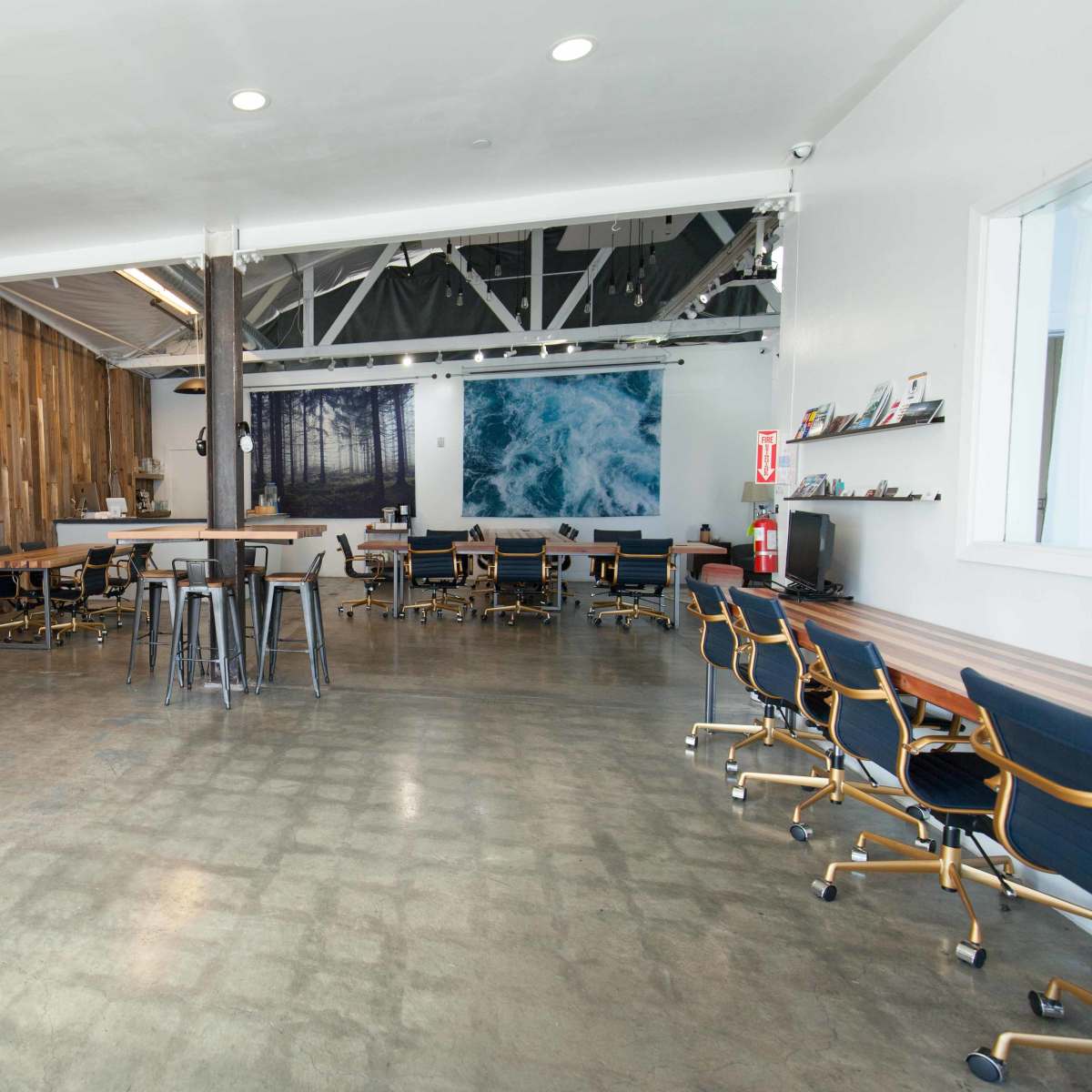 A modern office space with wooden walls, several tables and chairs, and a large mural of ocean waves.