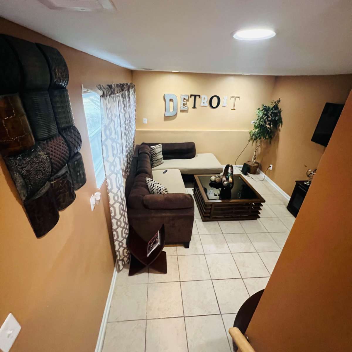 A cozy living room with a sectional couch, a coffee table, and decorative elements on the walls, including the word "Detroit."