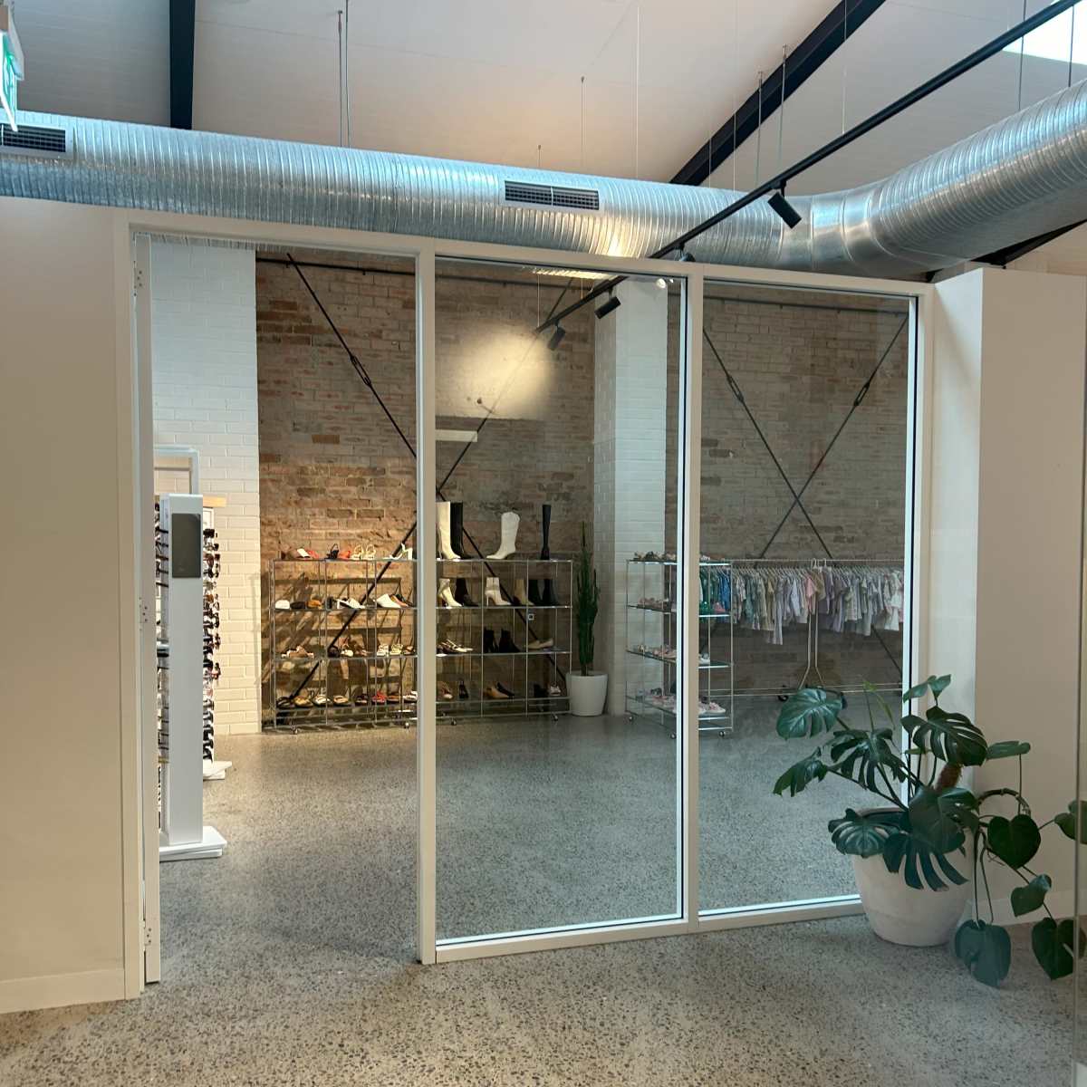 A modern retail space with a large glass partition, exposed brick walls, and displays of clothing and accessories in the background.