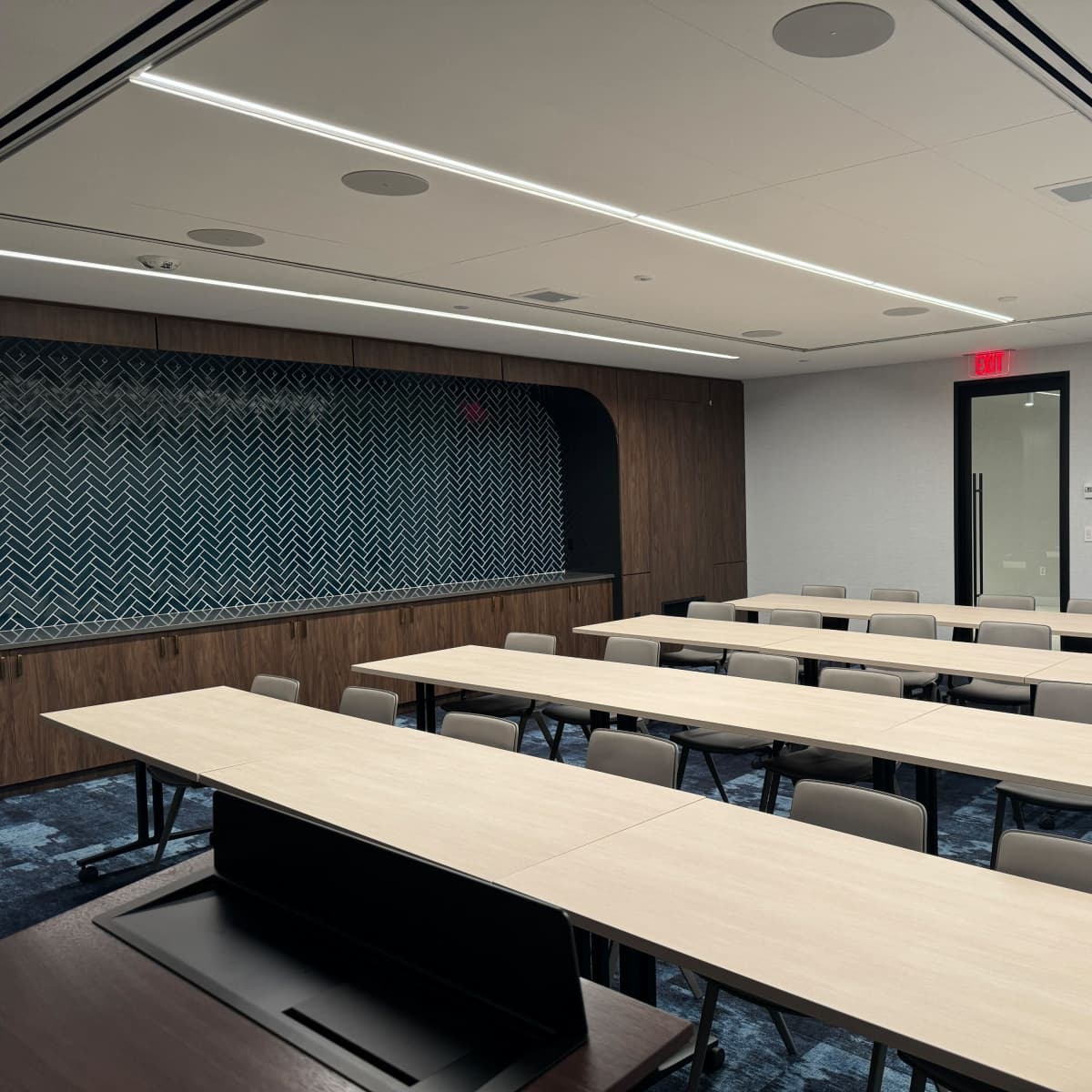 A conference room features several long rectangular tables arranged in rows, with chairs on either side and a patterned backdrop.